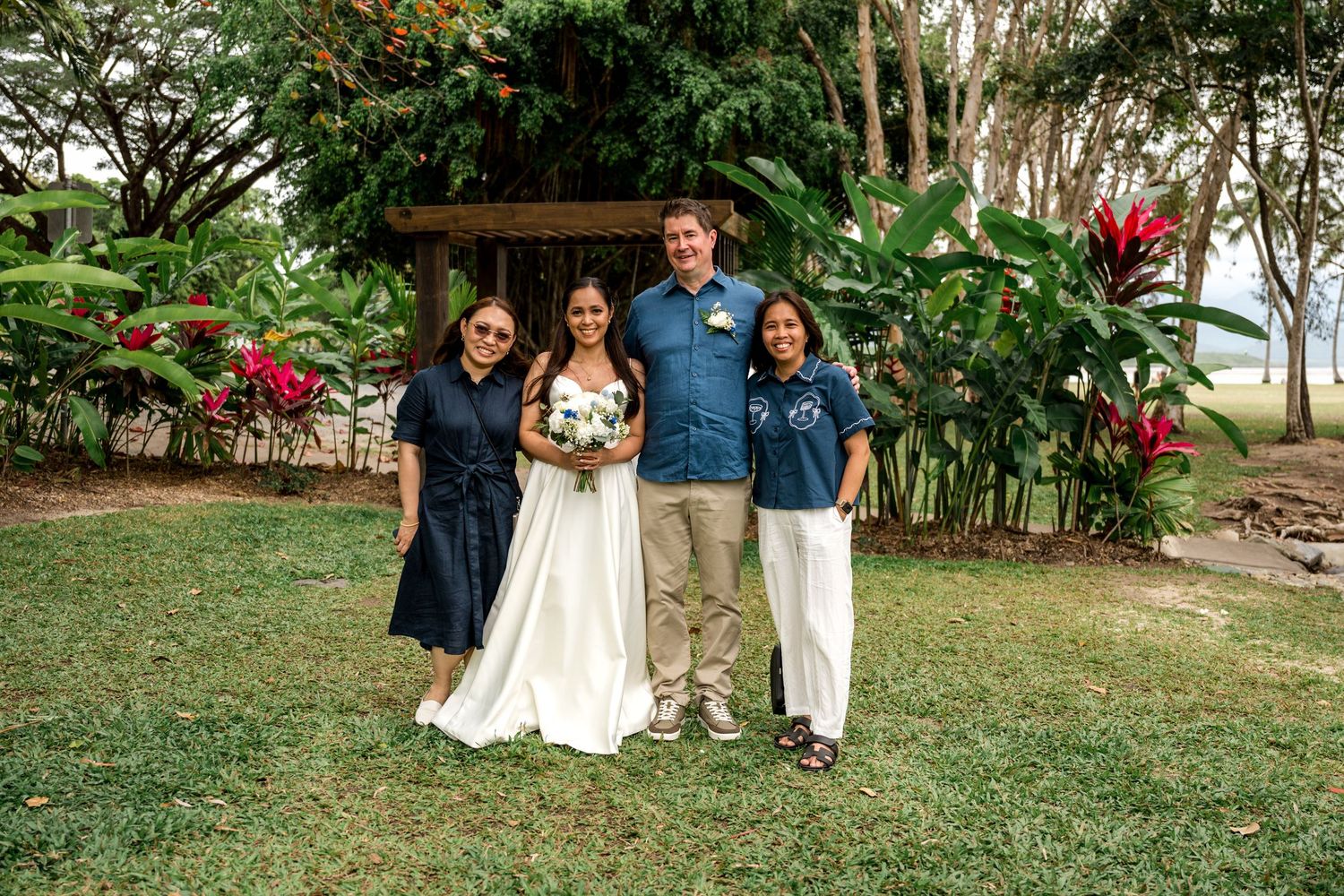 Bride holding bouquet poses with groom and two female guests in tropical garden setting at Little Cove, Port Douglas.