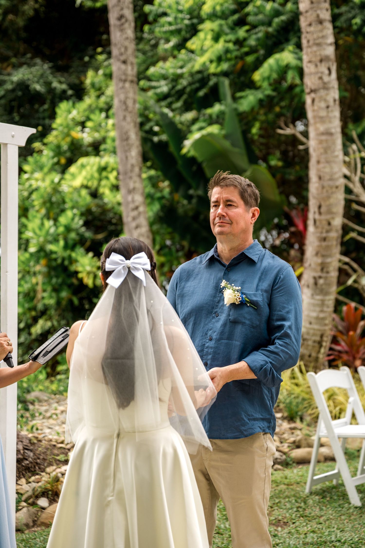 Groom smiles warmly at bride during outdoor wedding ceremony with lush tropical greenery in the background at Little Cove, Port Douglas.