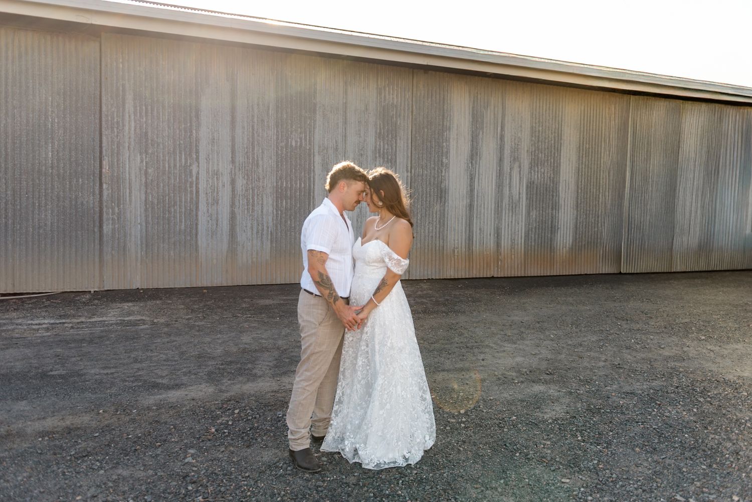 Bride and groom share an intimate forehead-to-forehead moment in warm sunset light before a corrugated metal wall.