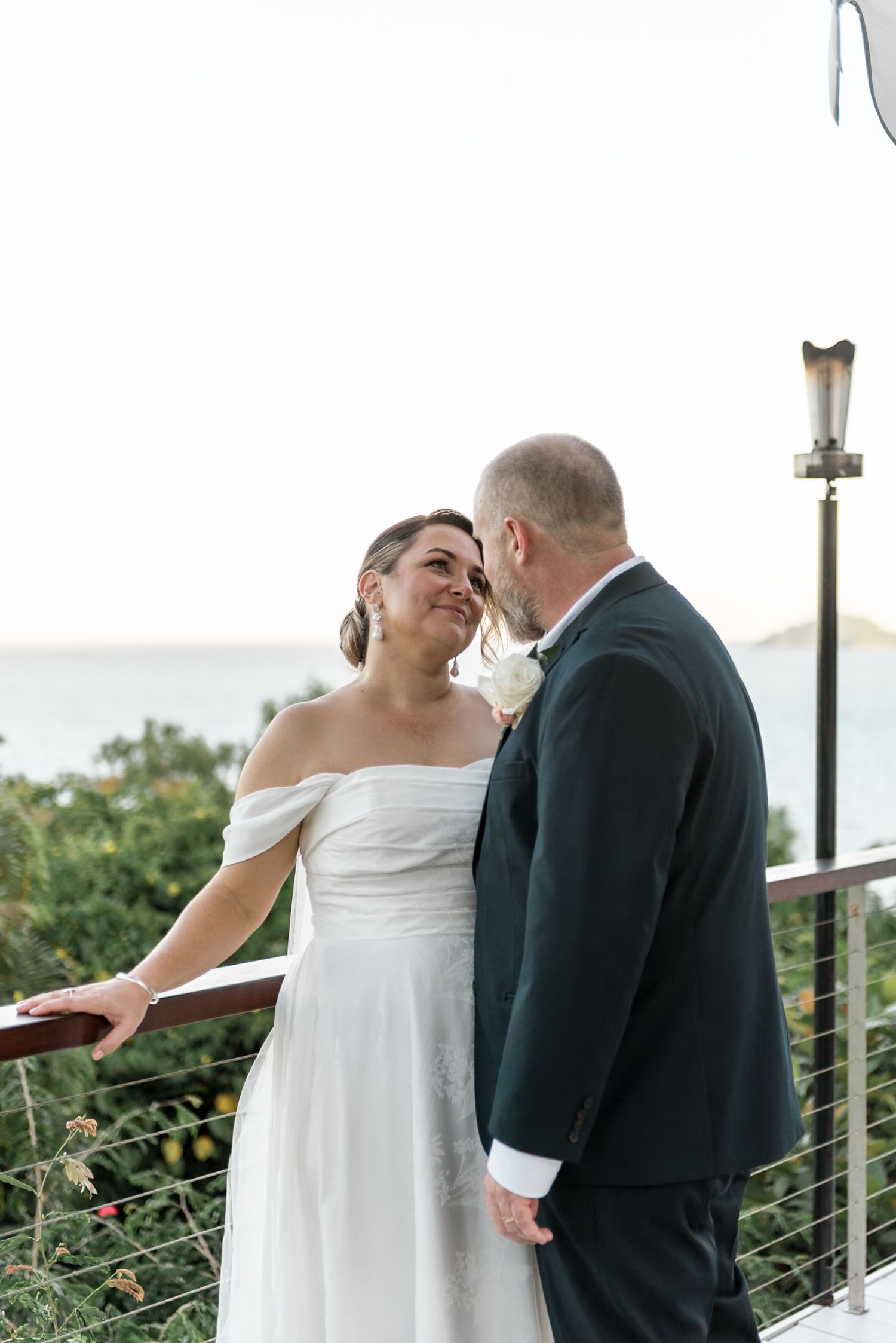 Bride and groom sharing an intimate moment on a balcony overlooking the ocean.