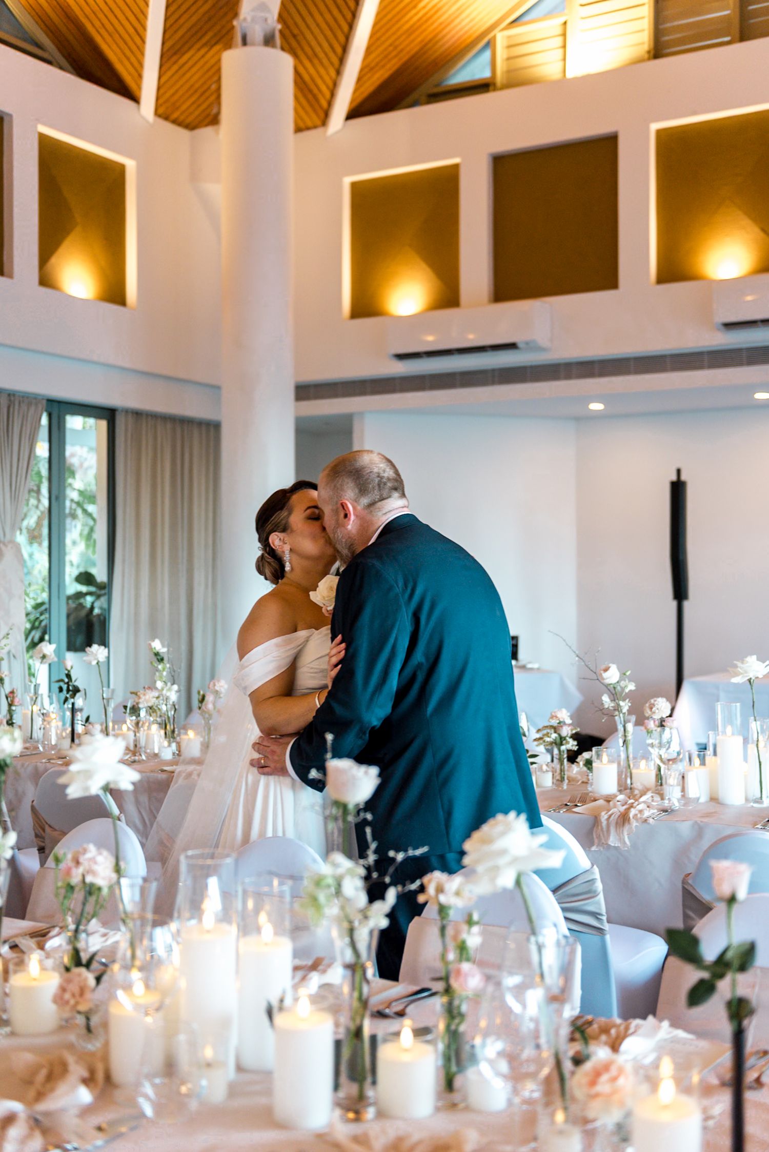 Bride and groom share a romantic kiss during their first dance at a candlelit wedding reception.
