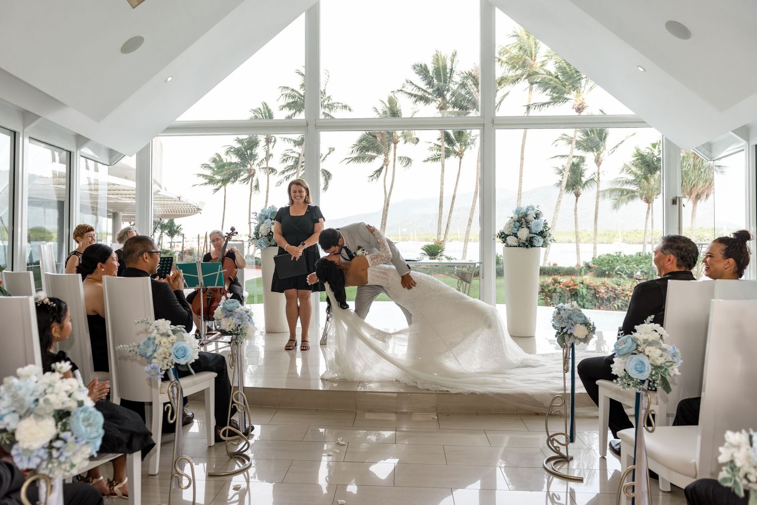 Bride and groom share first kiss at altar in stunning oceanfront wedding chapel with palm tree views.