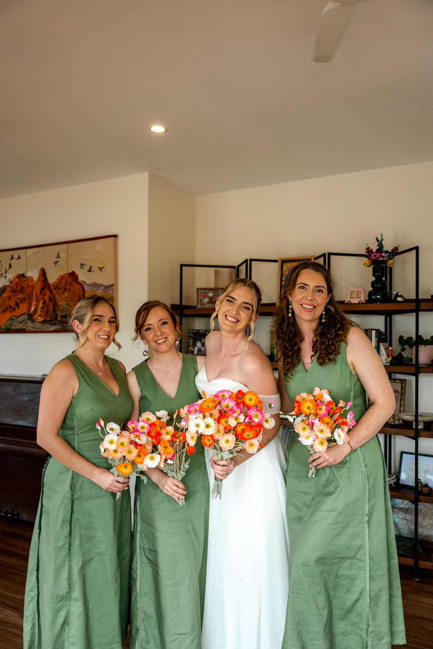 Bride in white gown laughs with three bridesmaids in green dresses holding colorful floral bouquets.