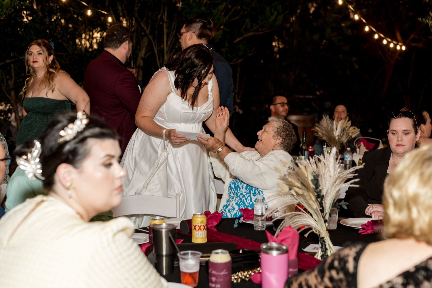 Wedding guests seated at decorated reception tables as bride greets attendees.