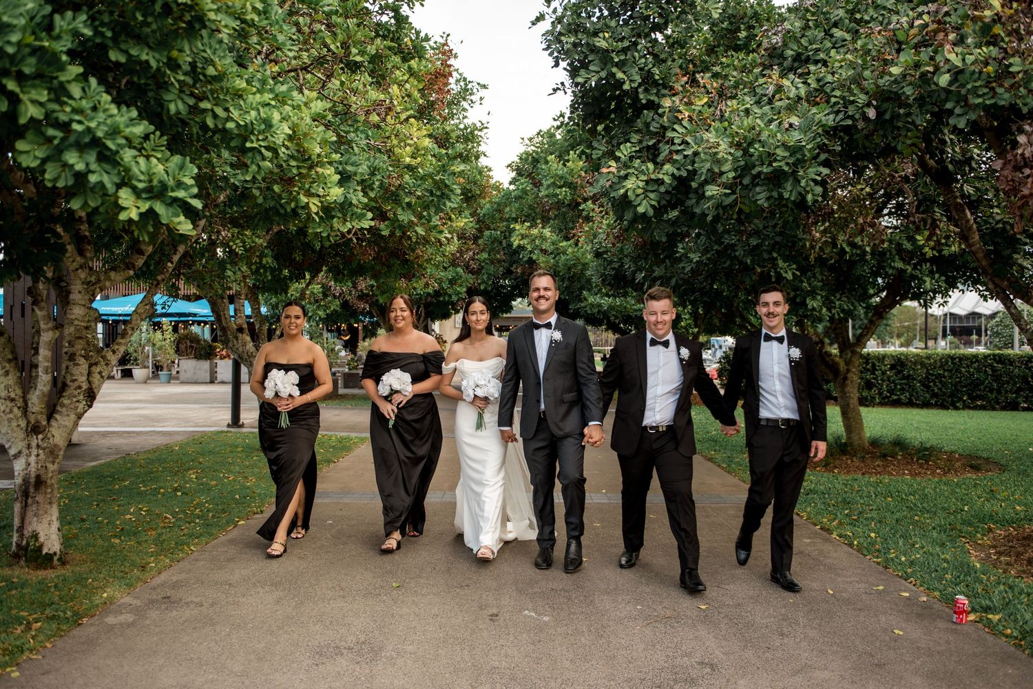 Bride and groom with bridal party strolling through a lush green park.
