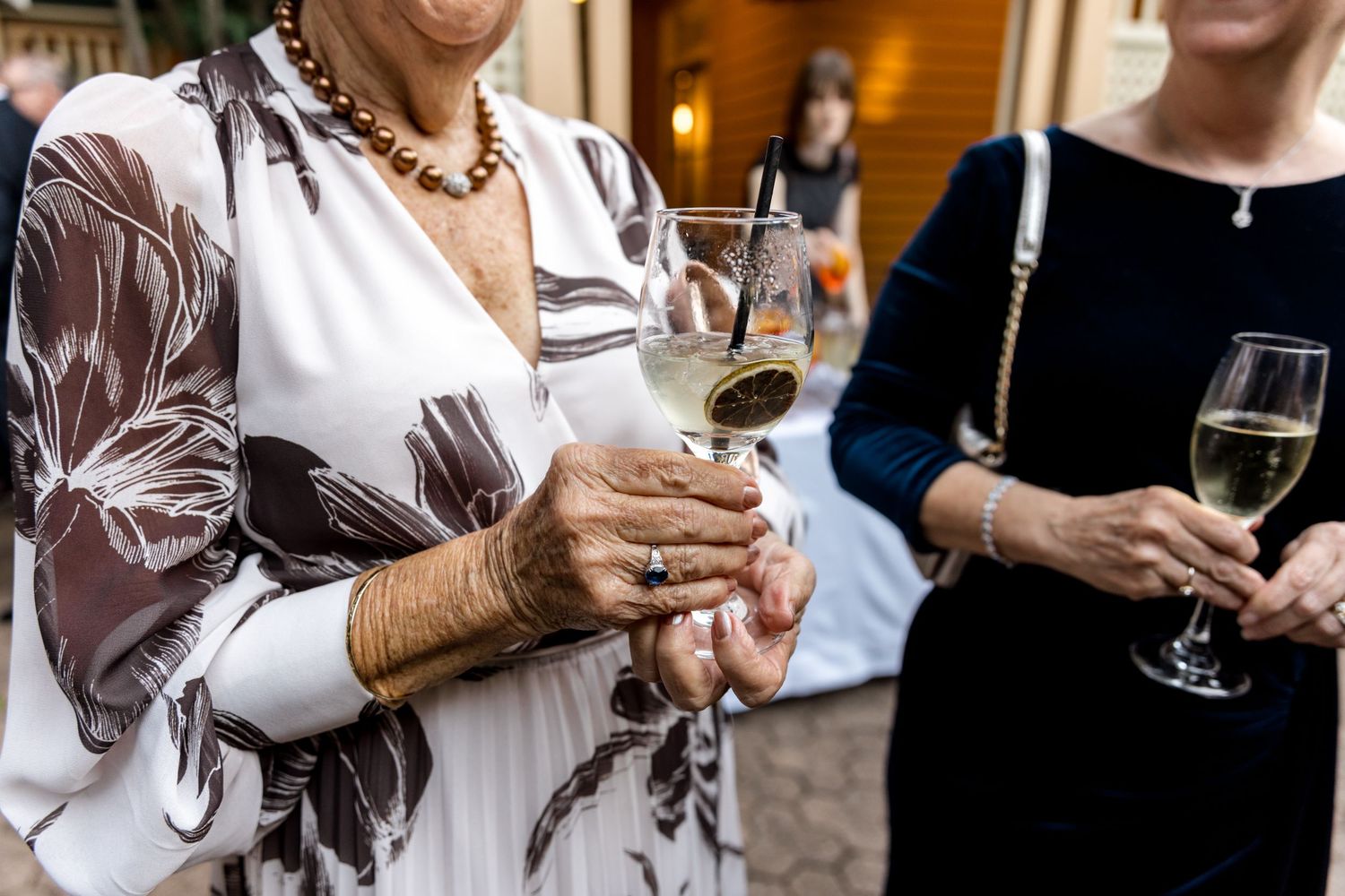 Two elegantly dressed women holding champagne glasses at a wedding reception outdoor event.