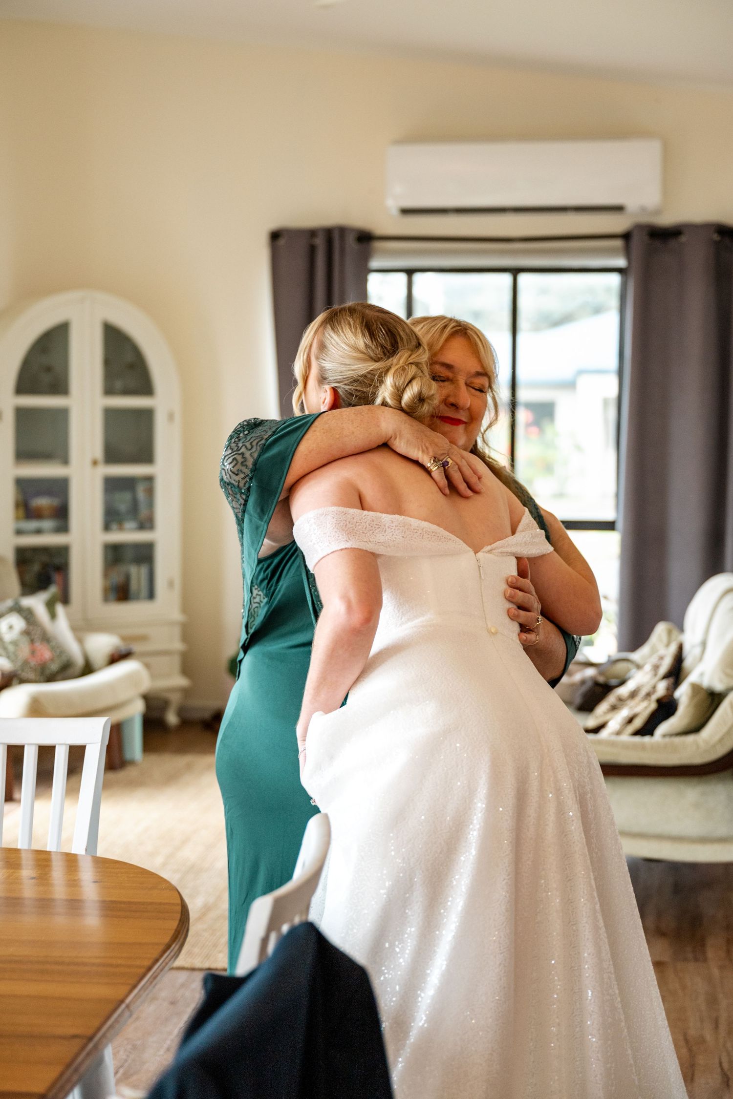 Mother and bride share a heartfelt hug during wedding morning preparations indoors.