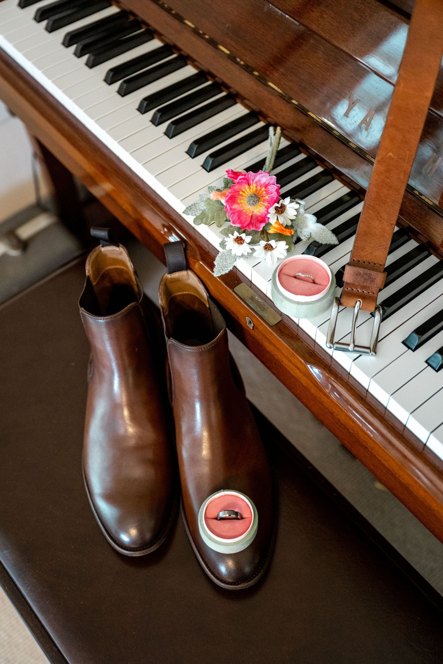 Brown leather Chelsea boots and wedding rings beside piano with floral bouquet decor.