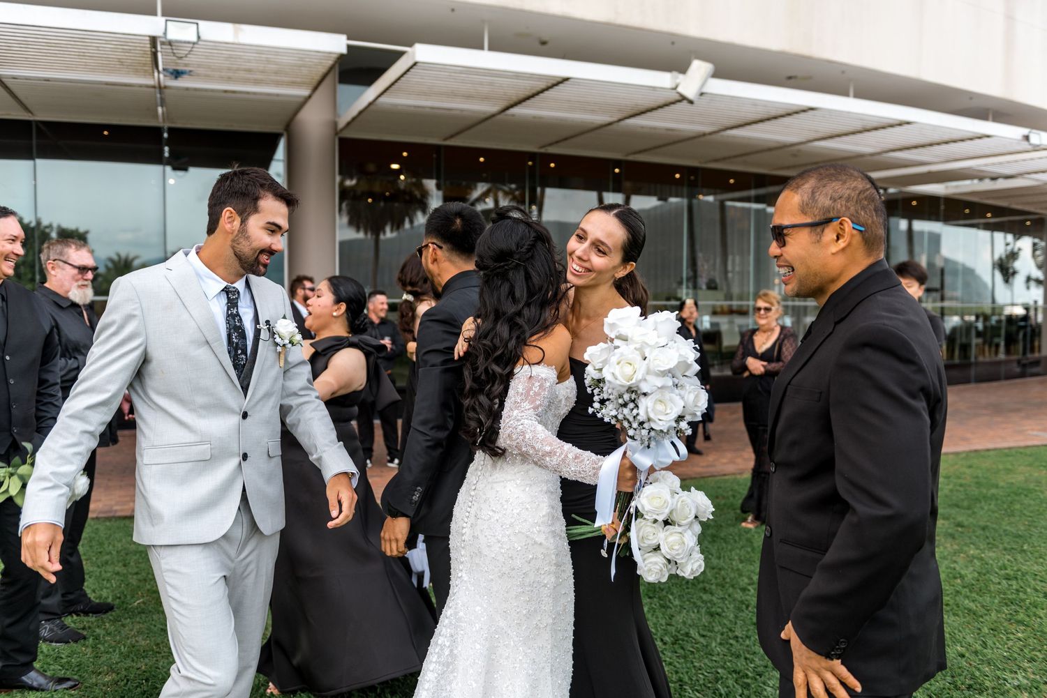 Bride and groom celebrate with family and friends on lawn outside elegant beachfront wedding venue.