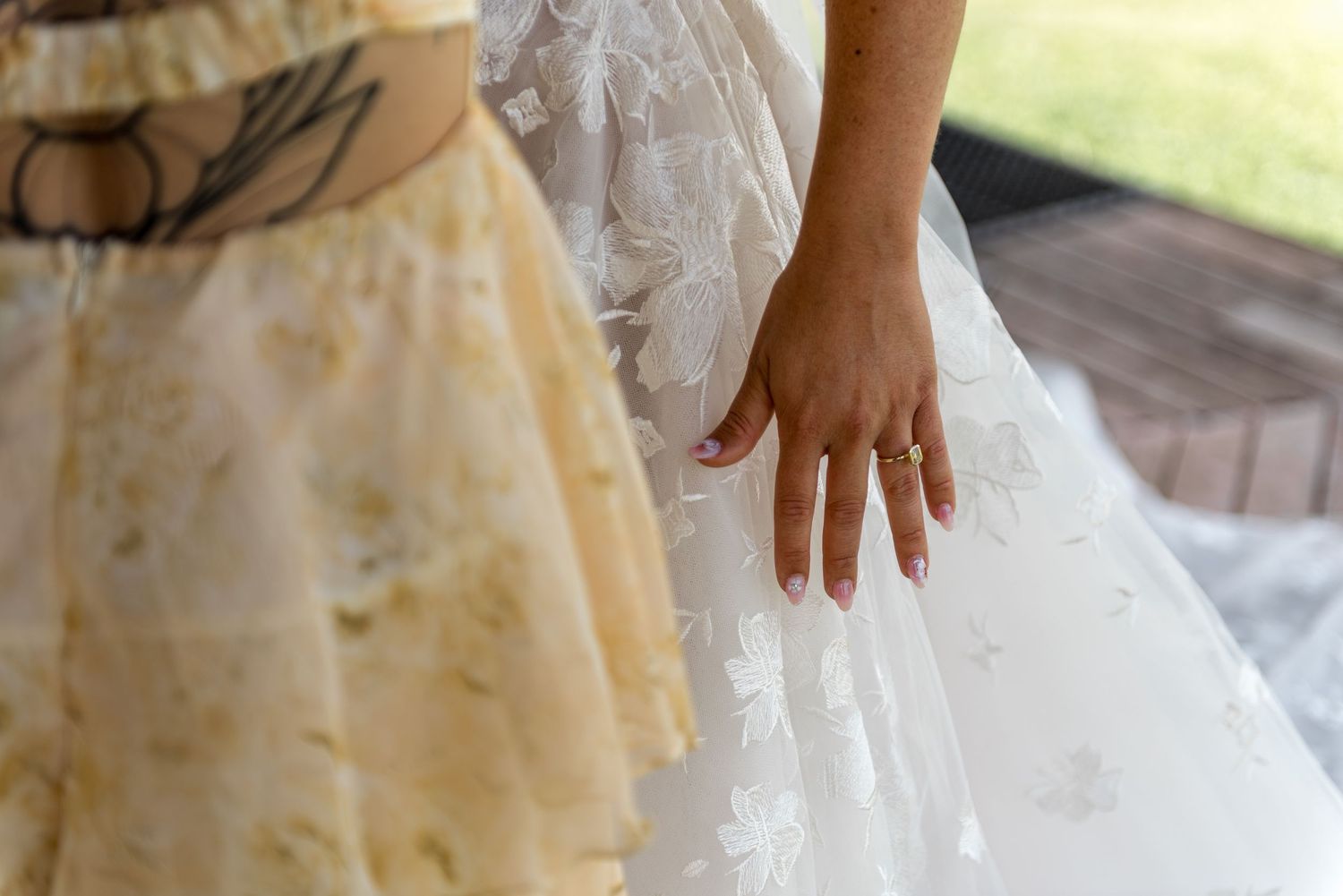 Close-up of bride's hand displaying engagement ring against white lace wedding dress fabric.