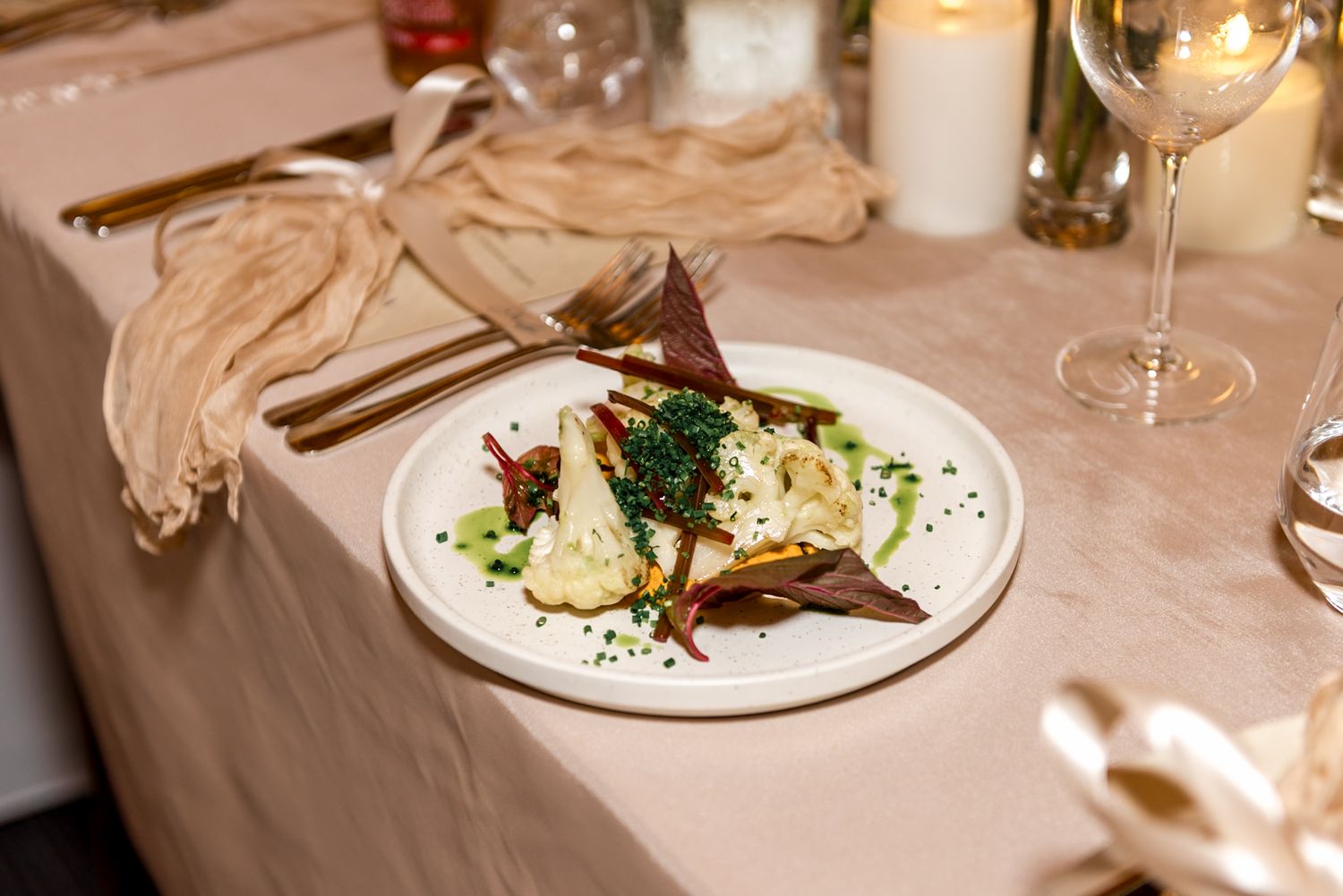 Elegant wedding reception plate with gourmet food garnished with herbs, served on white plate with gold cutlery.