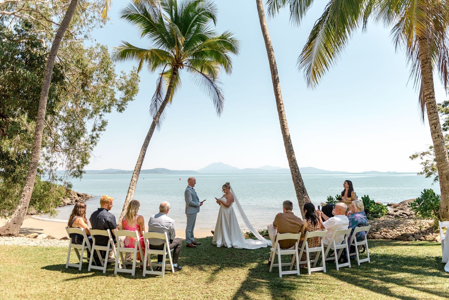 Picturesque tropical beach wedding ceremony under palm trees with turquoise ocean and island backdrop.