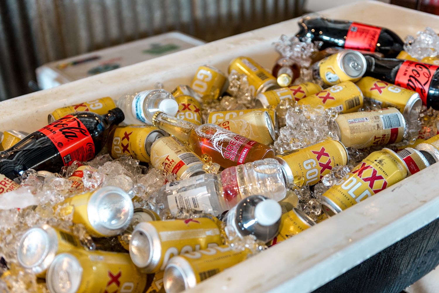 Assorted canned beverages and drinks chilling on ice in a wooden cooler box.