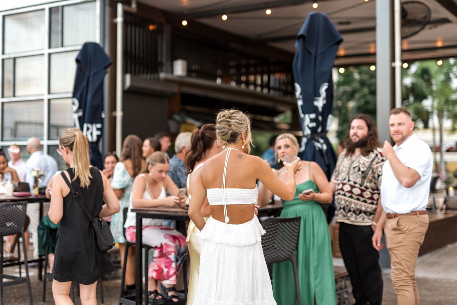 Bride in white backless dress mingling with wedding guests at outdoor reception venue.