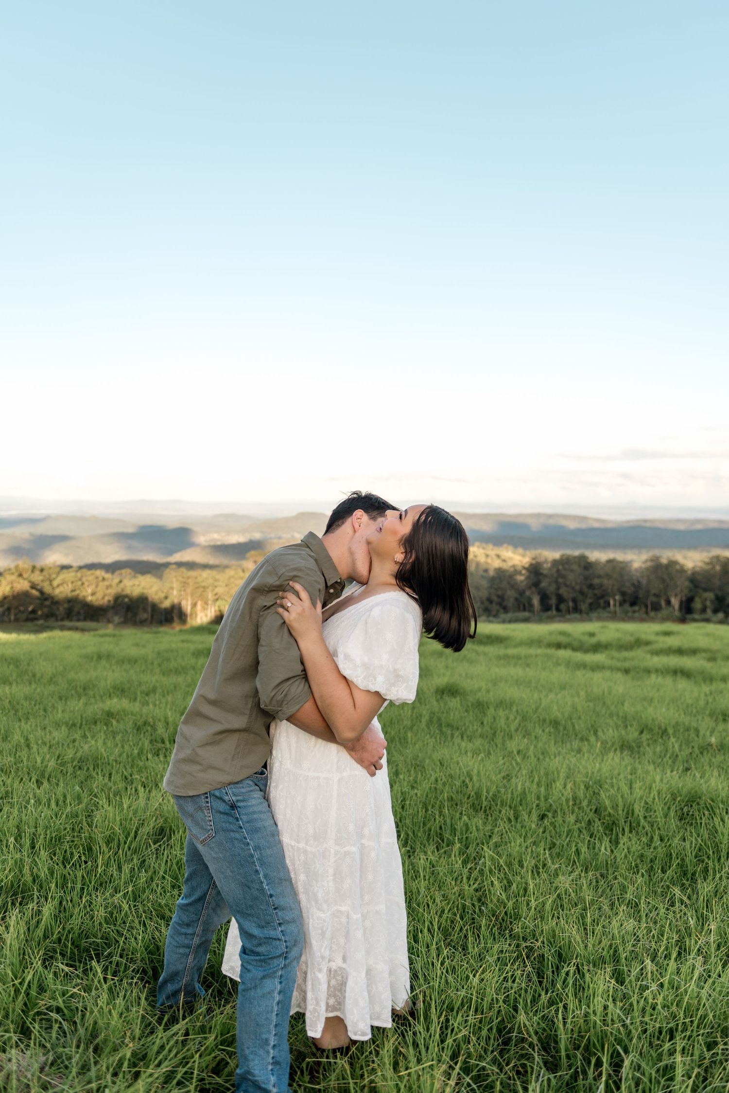 Couple sharing a passionate kiss in a vibrant green field at sunset.