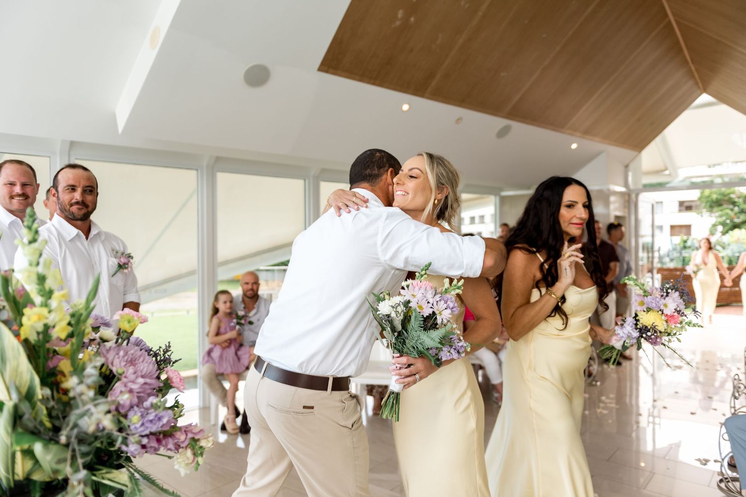 Groom embracing a bridesmaid in yellow dress during joyful wedding ceremony moment.