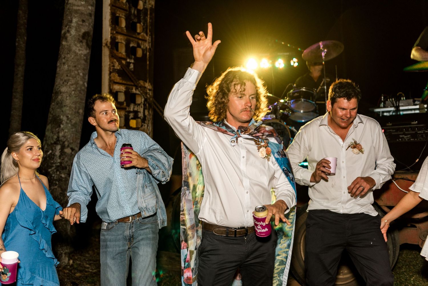 Group of men dancing energetically at an outdoor nighttime wedding party celebration.