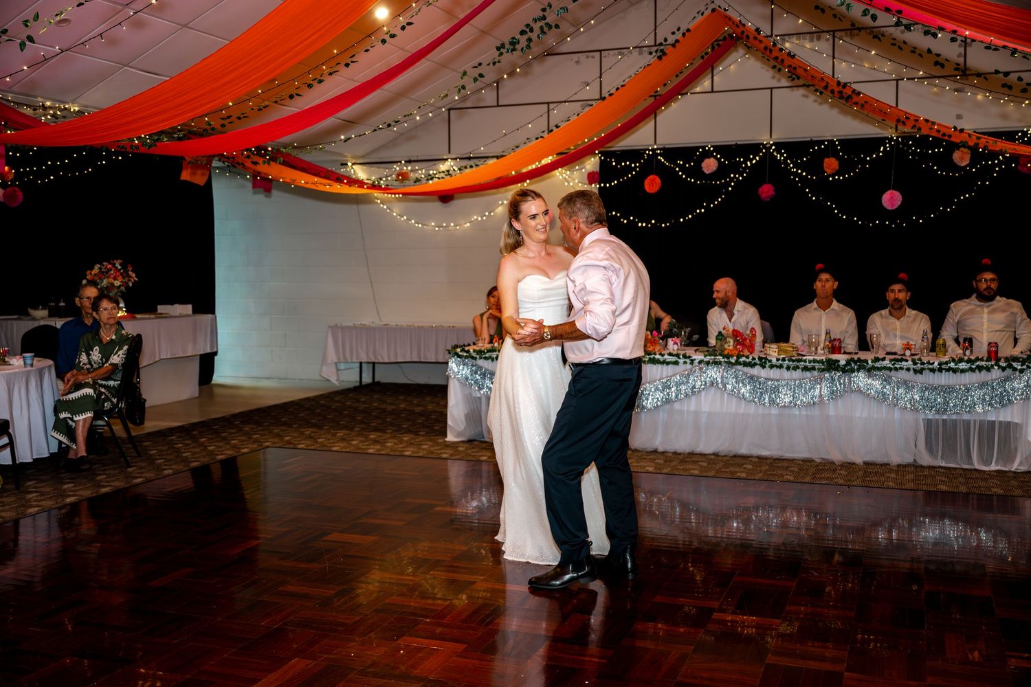 Bride and groom share a romantic first dance on wooden dance floor at elegantly decorated wedding venue.
