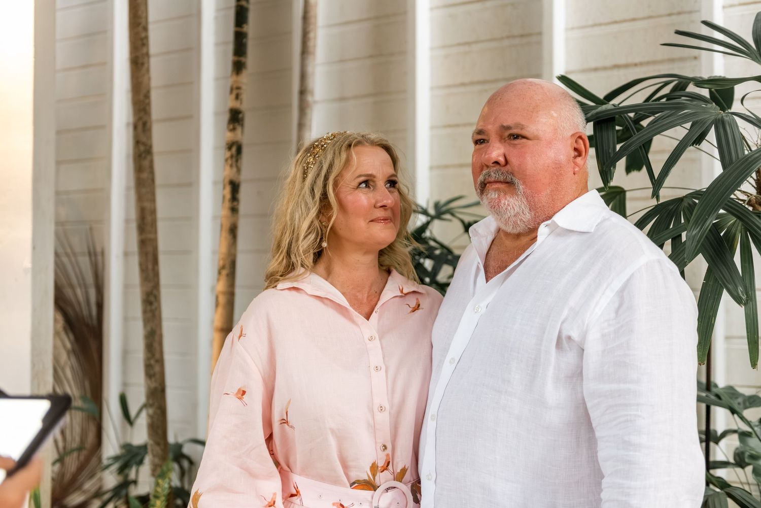 Mature couple sharing a tender moment surrounded by tropical greenery at an outdoor venue.