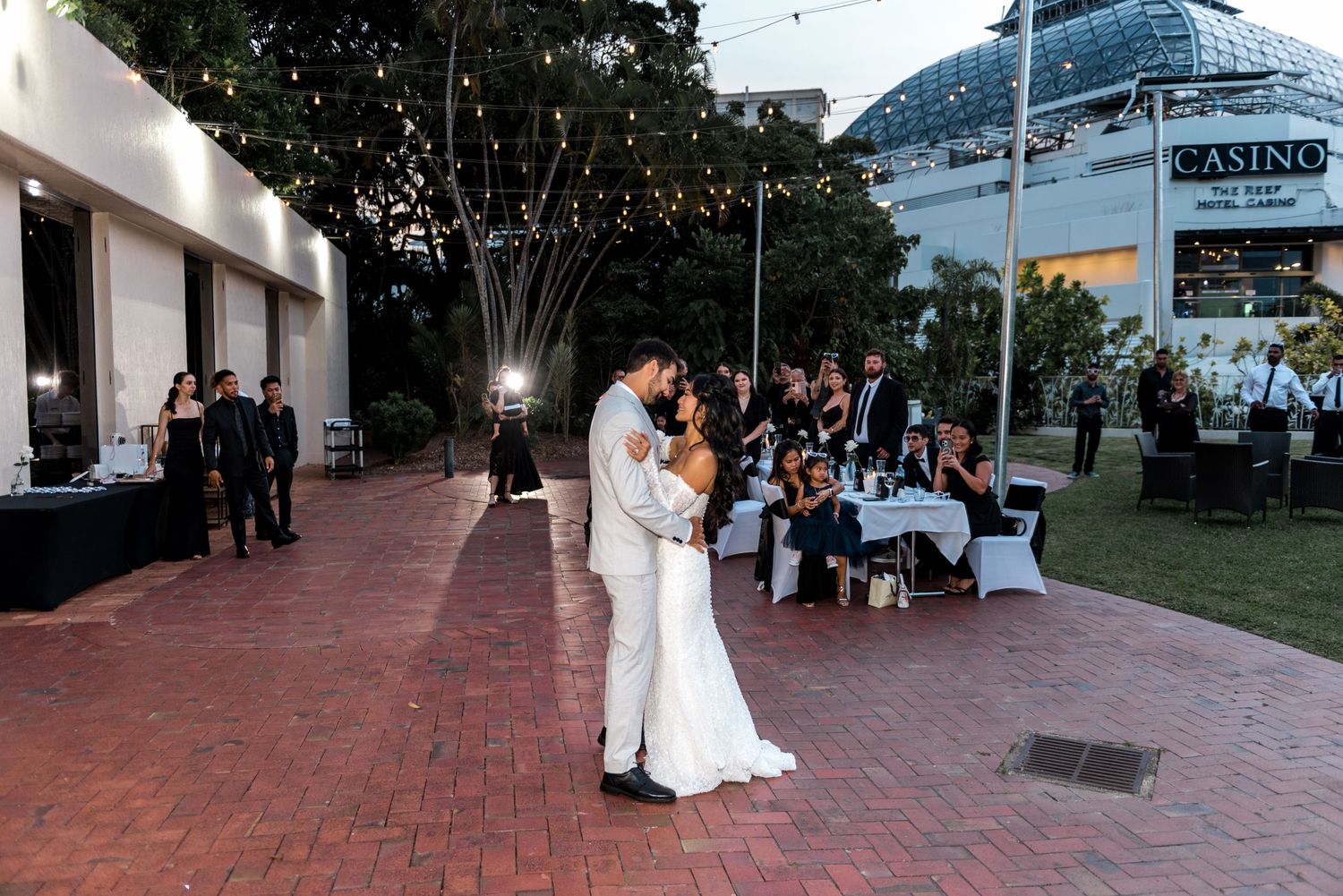 Bride and groom share their first dance outdoors at a wedding reception near a casino venue with string lights overhead.