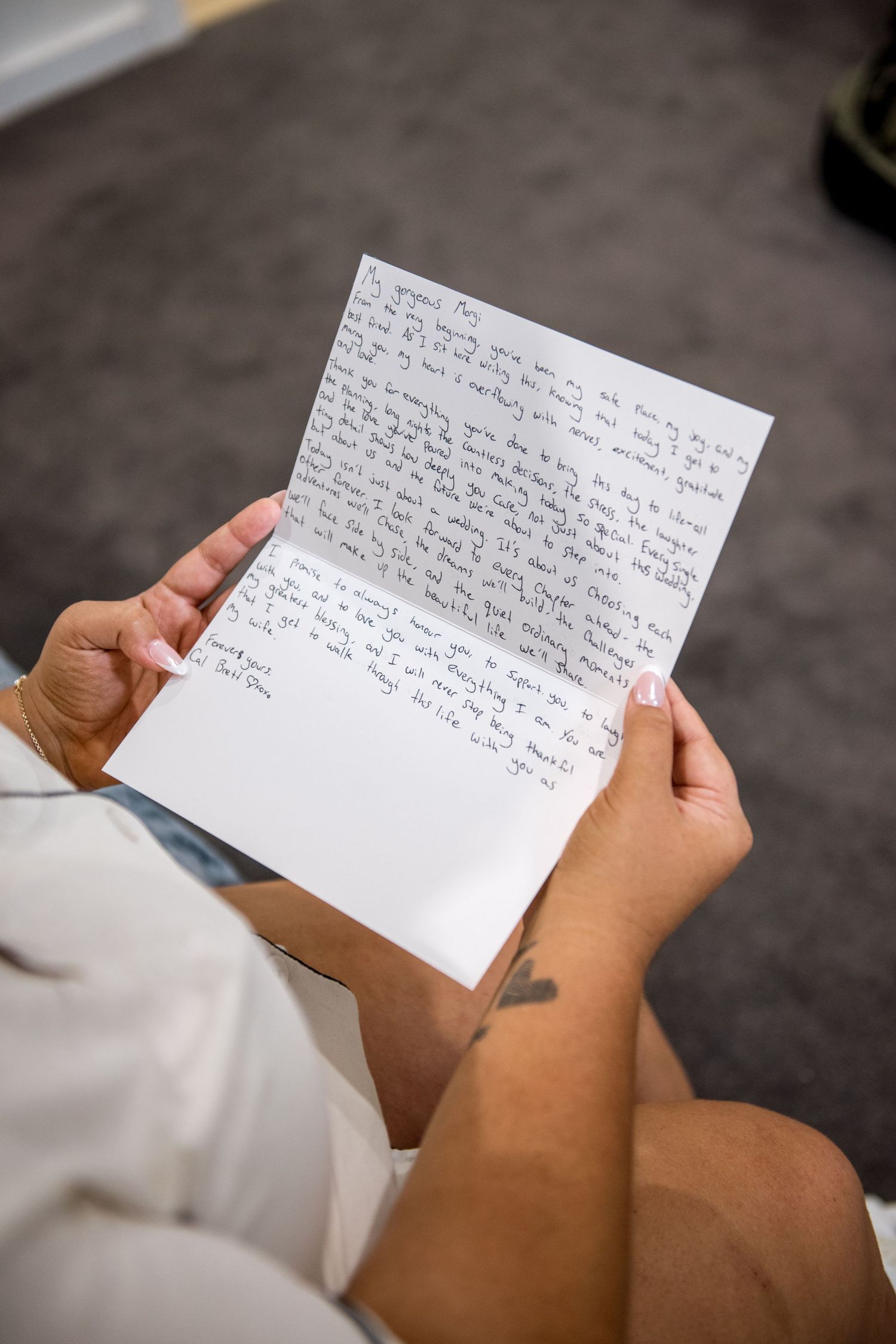 Close-up of hands holding a handwritten letter with a heart tattoo visible during wedding morning prep.
