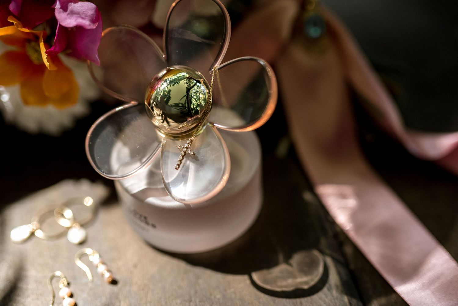 Gold flower-shaped brooch with green gemstone center displayed near a white candle and pink ribbon.