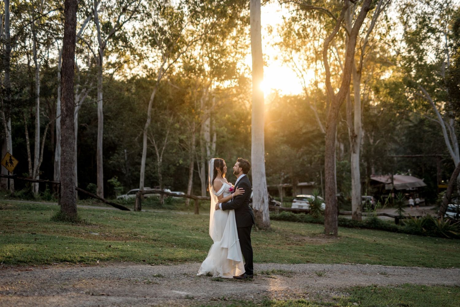 Bride and groom embrace at golden sunset in a wooded outdoor wedding setting.