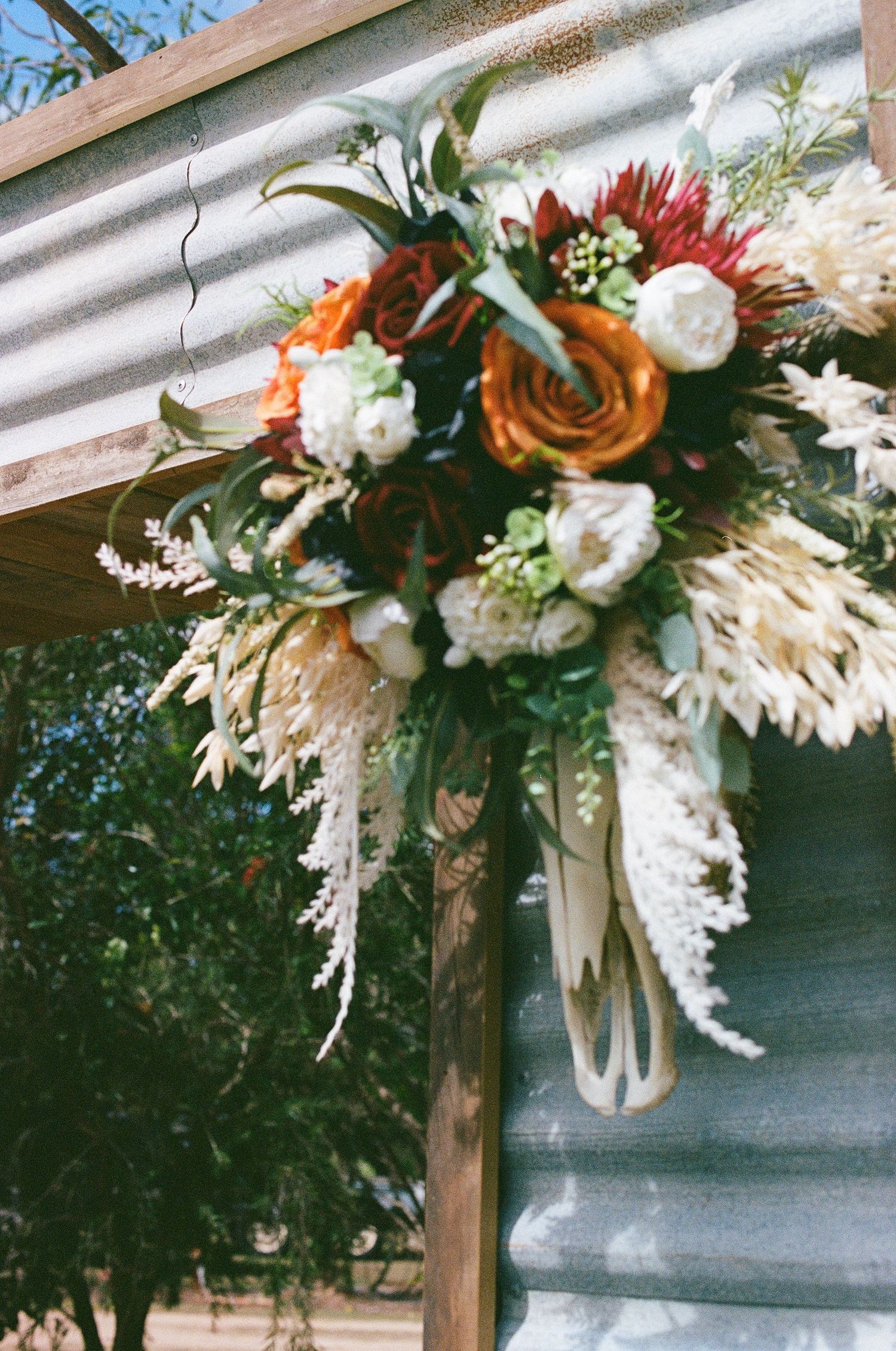 Rustic boho wedding arch decorated with orange, red, and white flowers with cascading white blooms.
