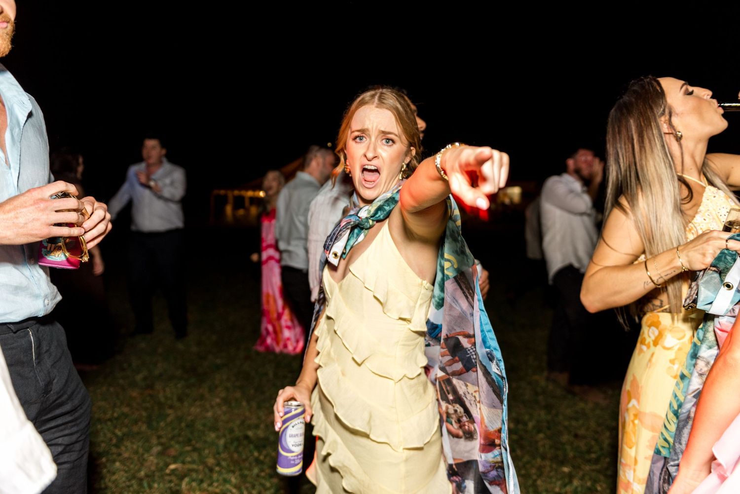 Woman in khaki outfit dancing enthusiastically at an outdoor evening wedding reception.