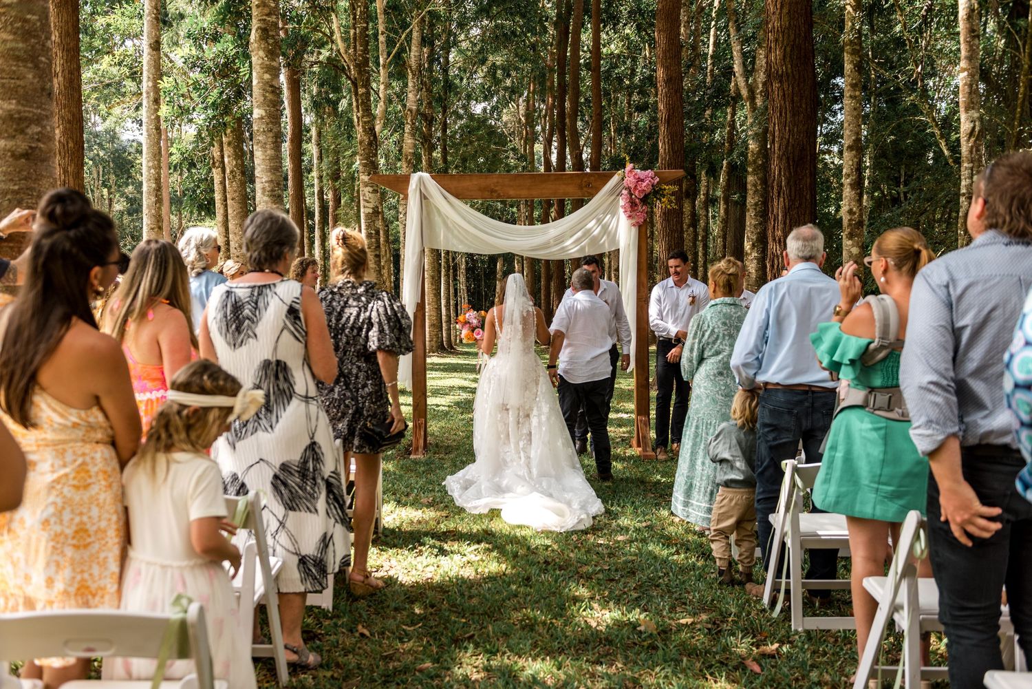 Bride approaching a wooden arch altar in an elegant outdoor forest wedding ceremony.
