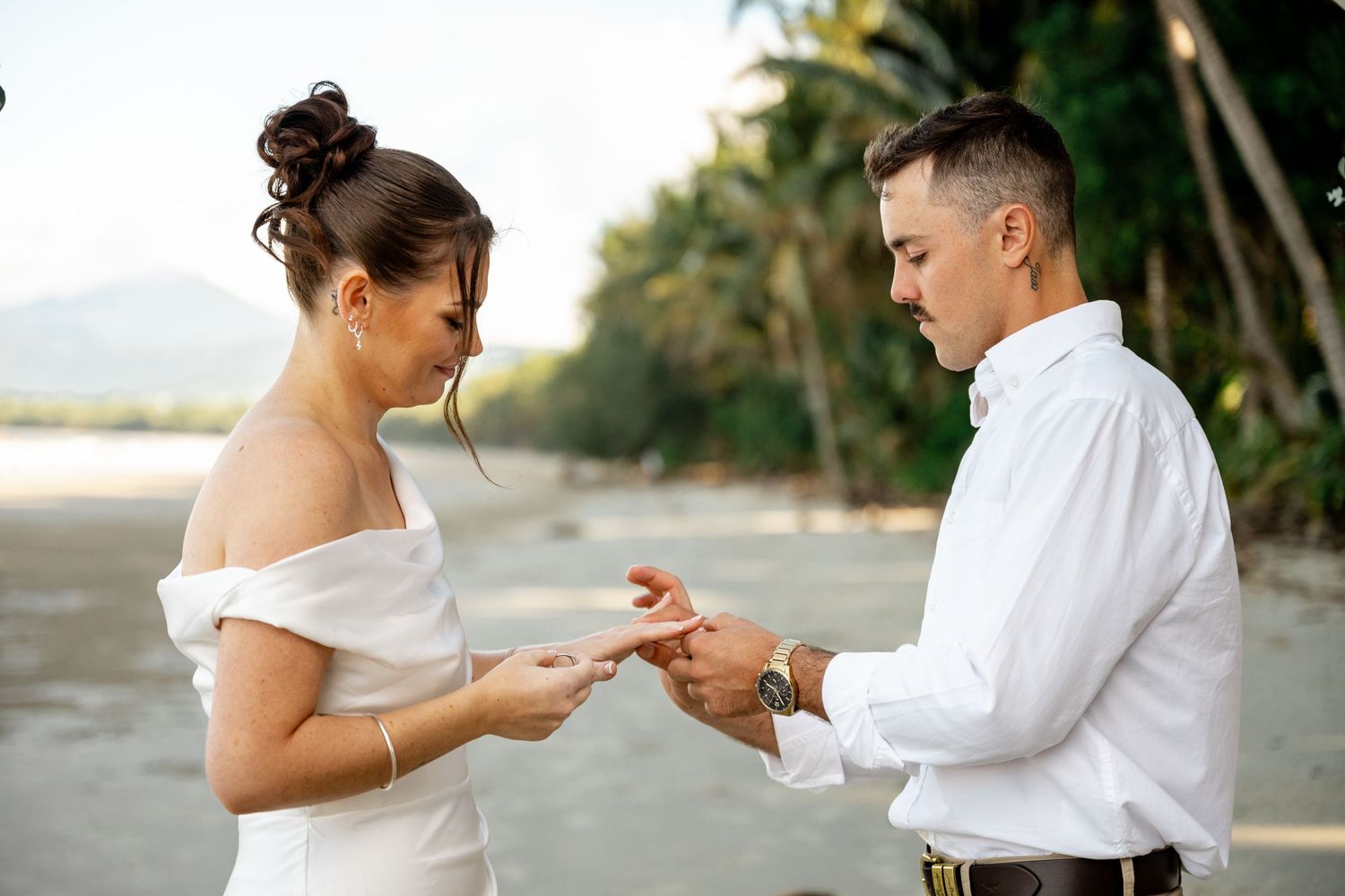 Groom placing a wedding ring on the brides finger during an intimate beach ceremony at sunset at Four Mile Beach, Port Douglas.
