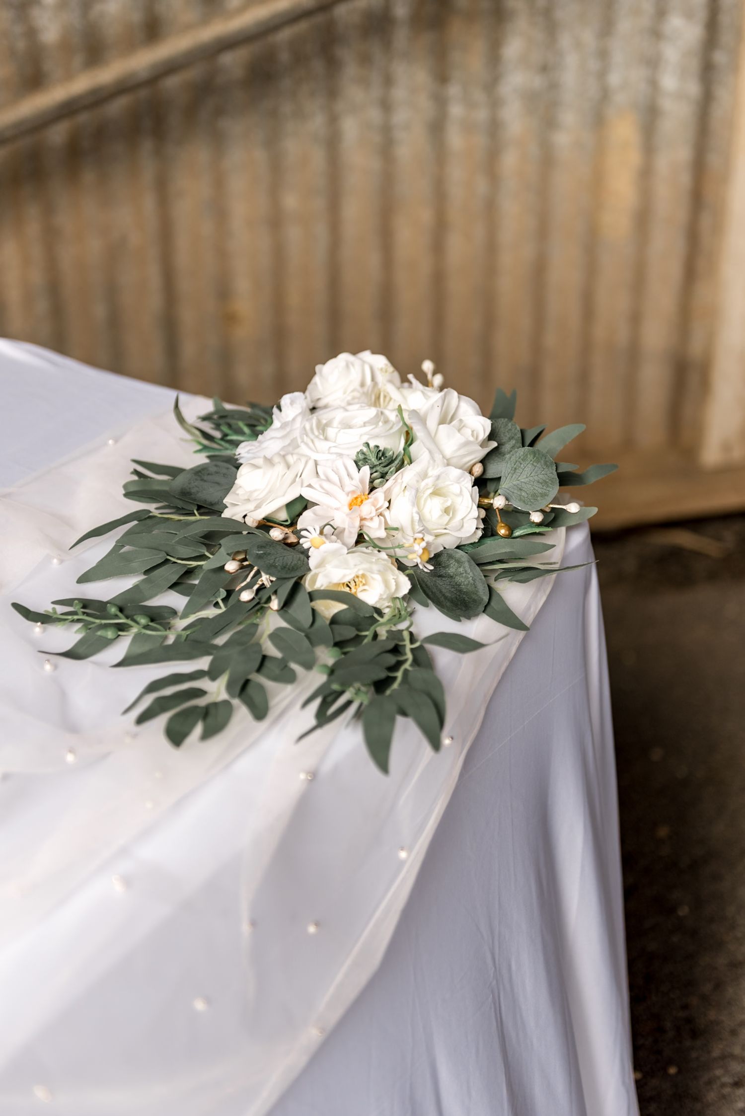 White rose and eucalyptus floral arrangement on a white tulle draped table.
