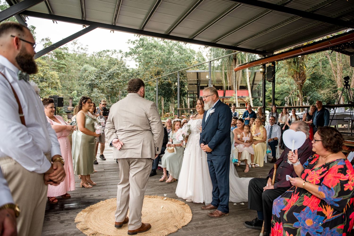 Wedding ceremony on outdoor pavilion with groom awaiting bride walking down the aisle.
