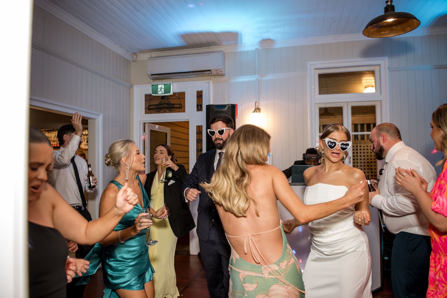 Wedding guests dancing and celebrating on the dance floor at a lively indoor wedding reception party.
