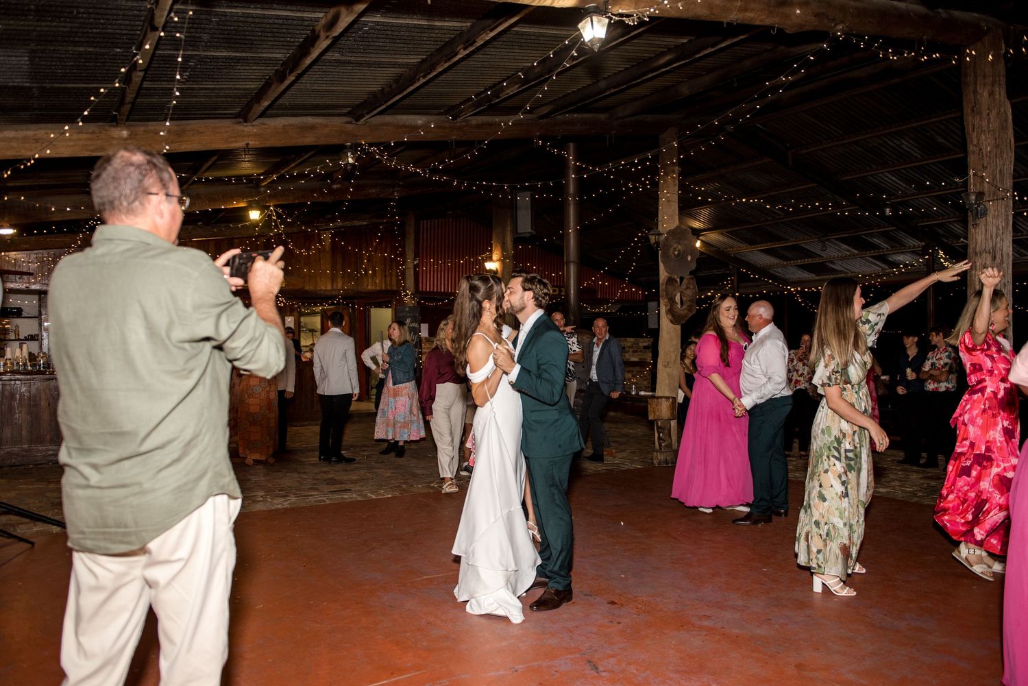 Wedding guests dance and celebrate with the bride and groom in a rustic barn.