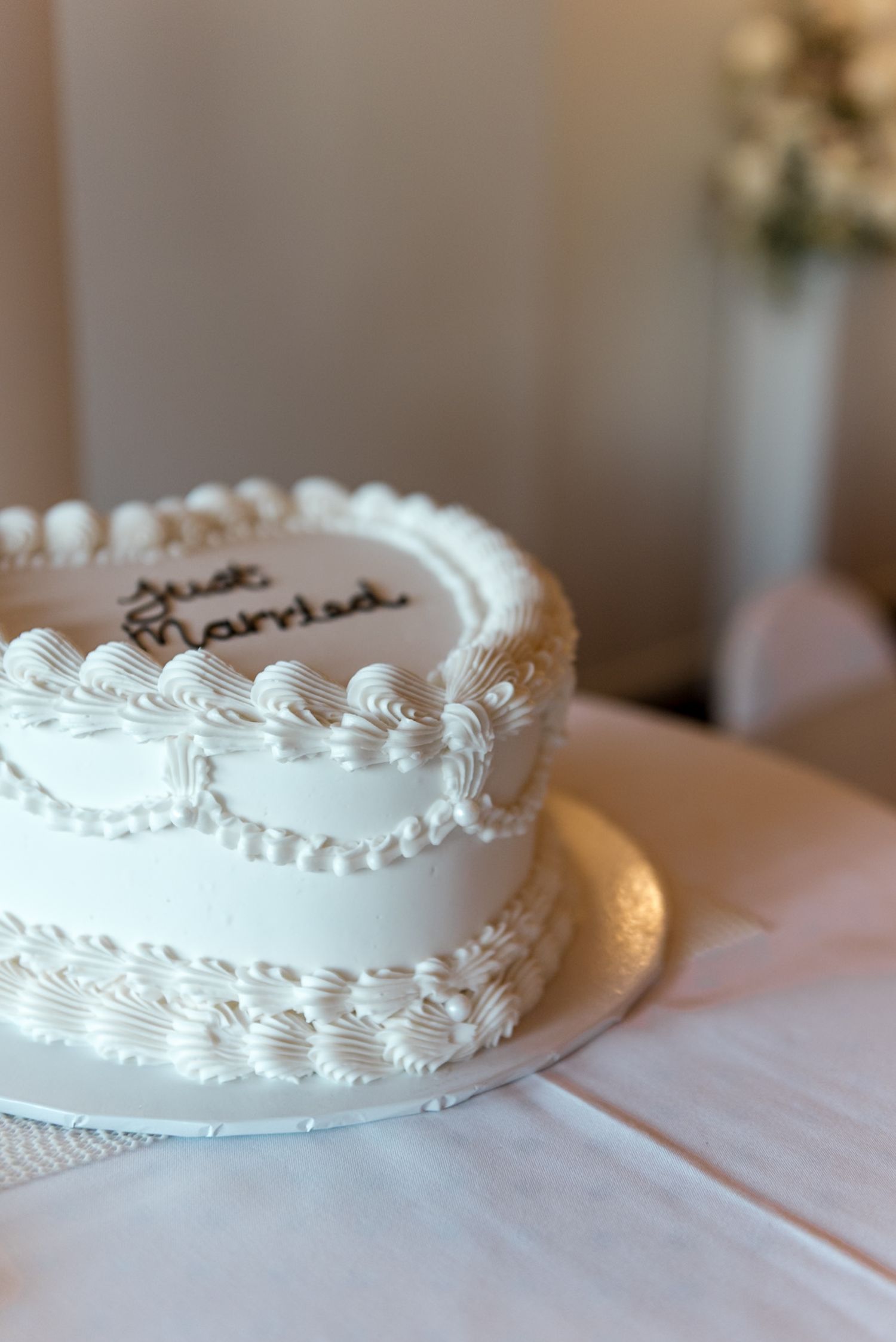 Close-up of a white heart-shaped wedding cake with Just Married written in black cursive frosting.