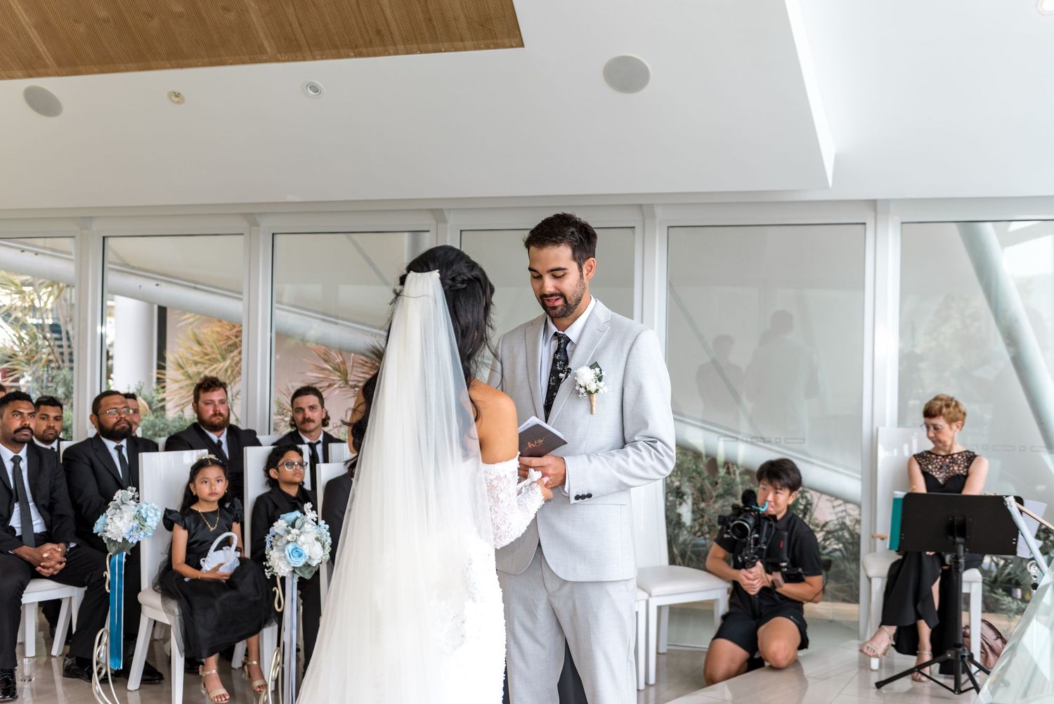 Bride and groom exchanging vows at elegant indoor wedding ceremony with seated guests watching.