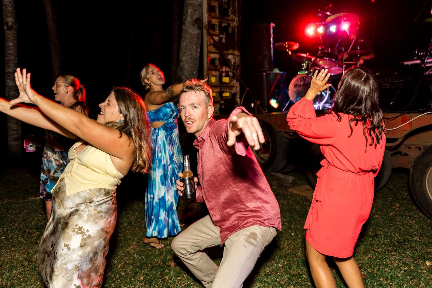 Guests dancing energetically at an outdoor wedding reception with colorful stage lights illuminating the night.