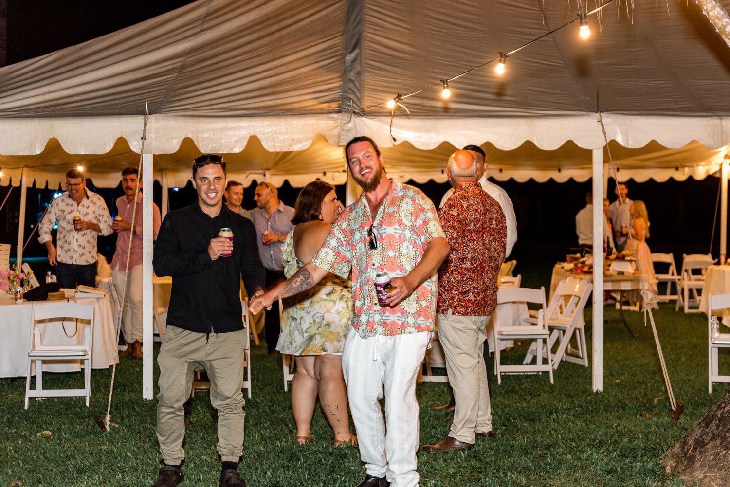 Wedding guests in colorful attire socializing under decorated tent at outdoor reception.