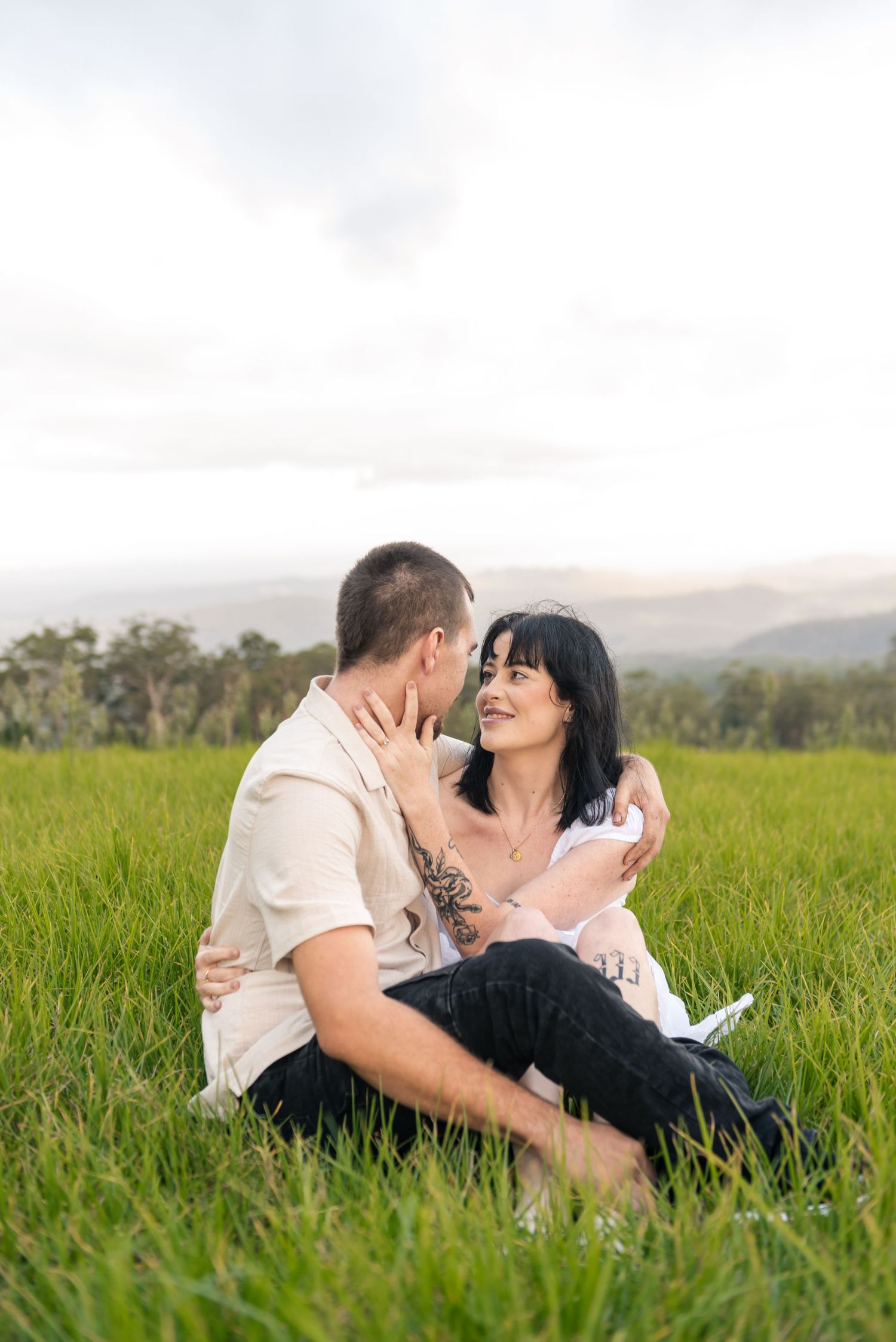 Couple sitting intimately in green grass field sharing a romantic moment together.