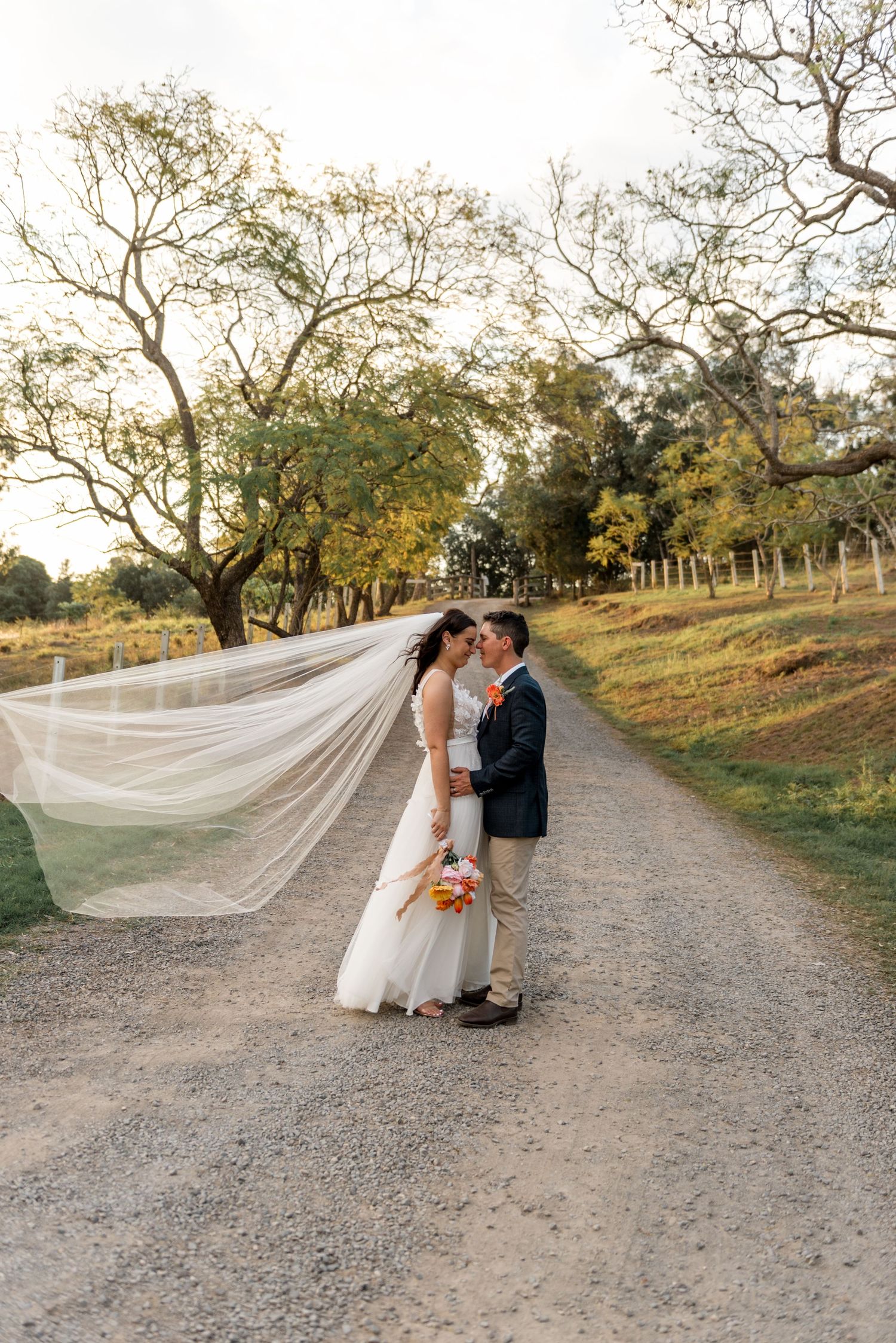 Bride and groom kissing on a gravel path with the bride's veil flowing dramatically in the wind.