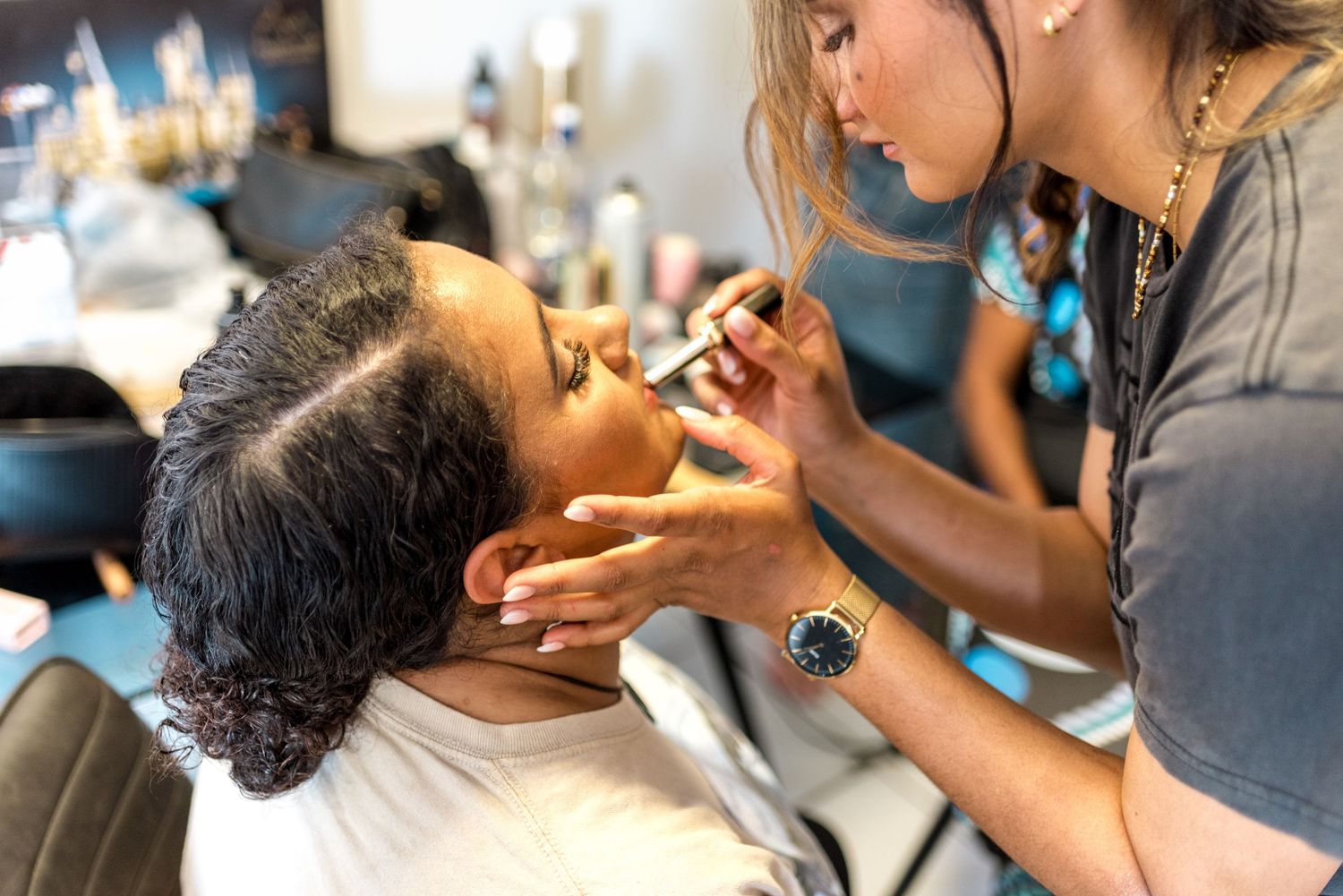 Close-up of makeup artist applying lipstick to bride in salon chair.