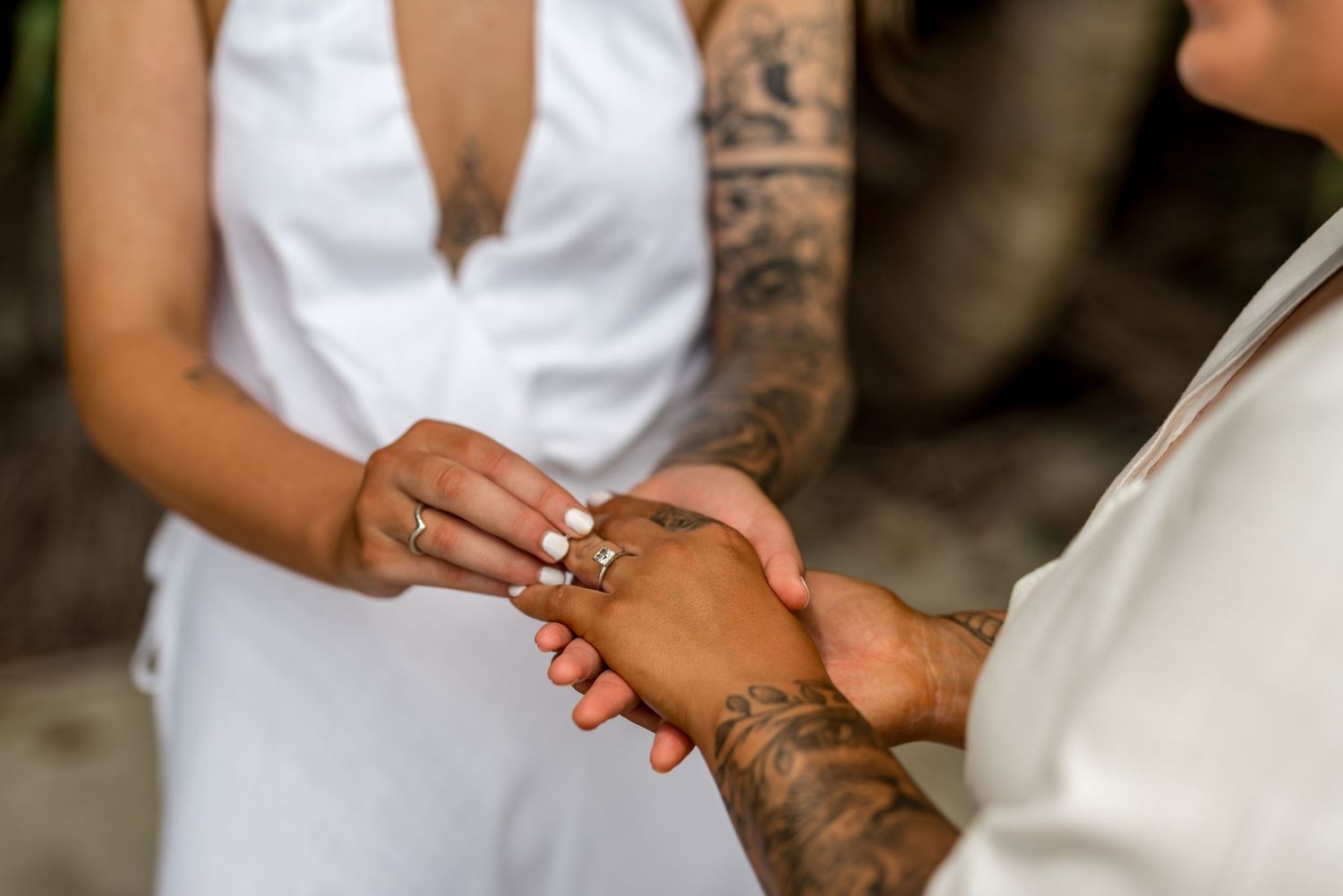 Close-up of tattooed bride receiving wedding ring during an intimate tropical beach ceremony.