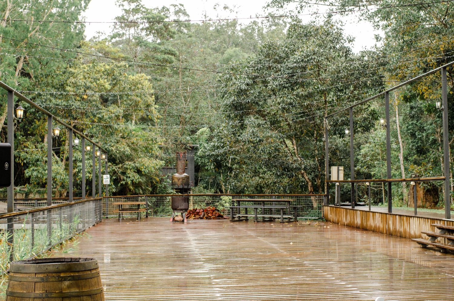 Rustic outdoor wedding venue with wooden dance floor surrounded by lush green trees in the rain.