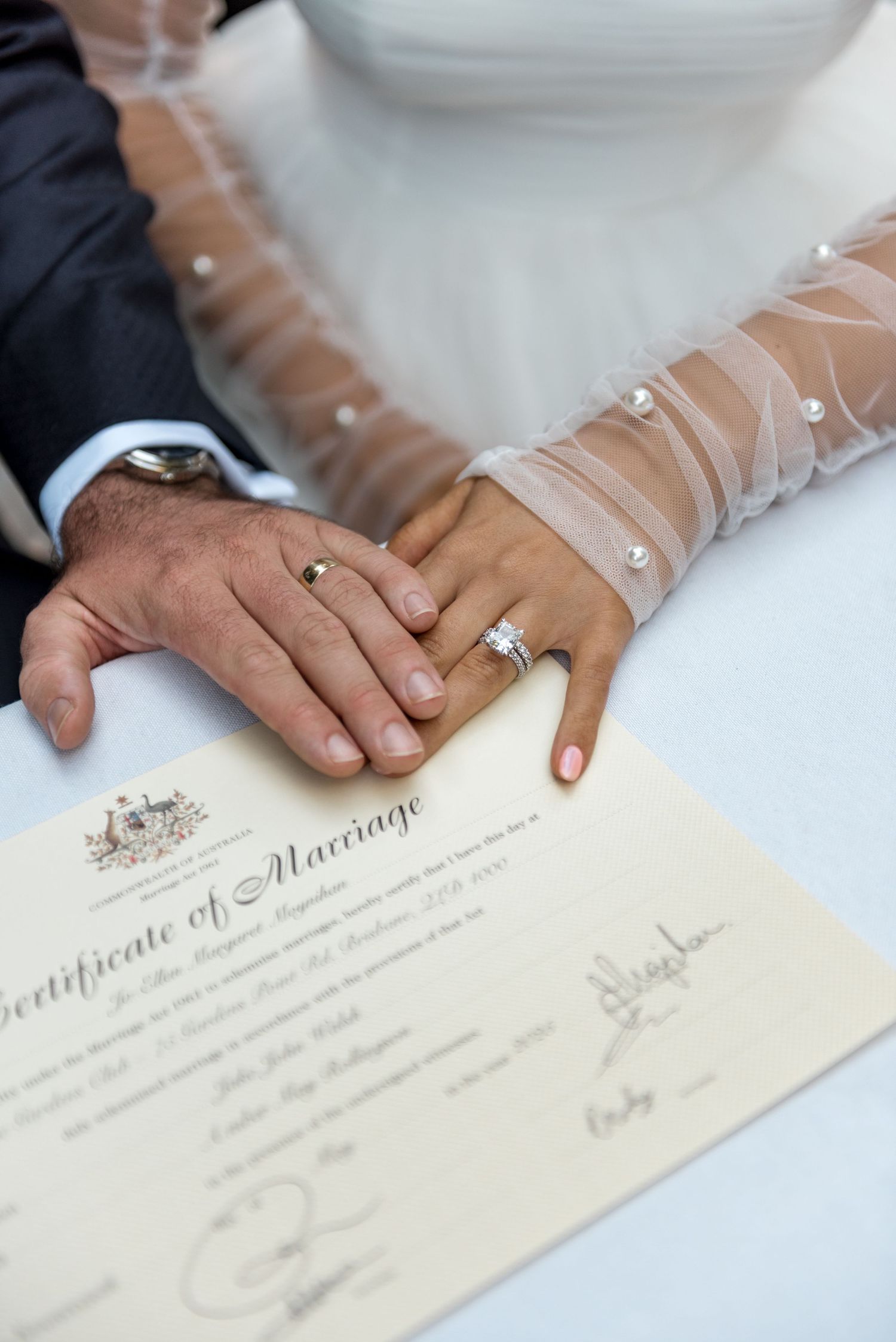 Bride and groom place hands on Australian Certificate of Marriage, showcasing wedding rings.