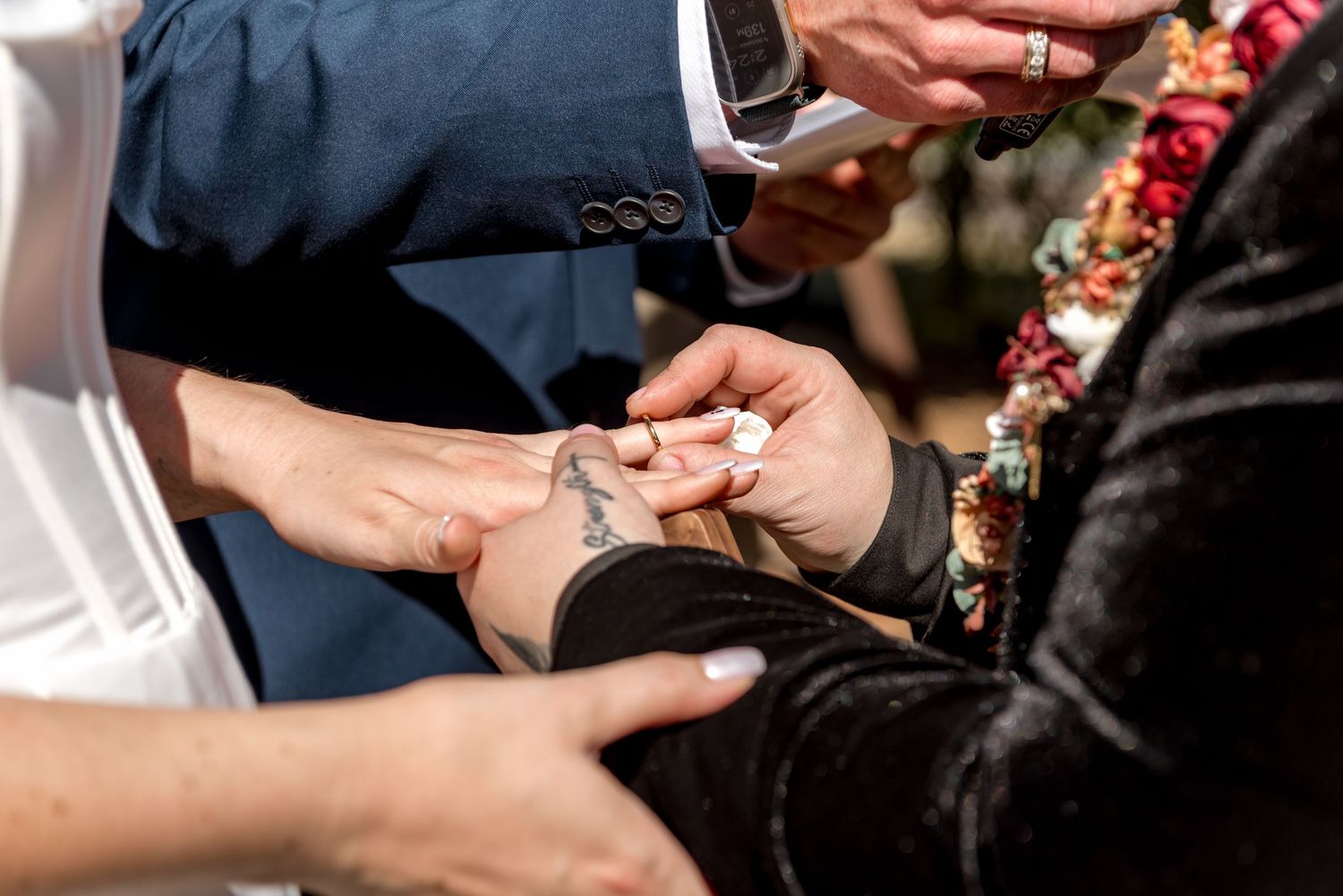 Close-up of wedding ring exchange with tattooed hands during outdoor ceremony.