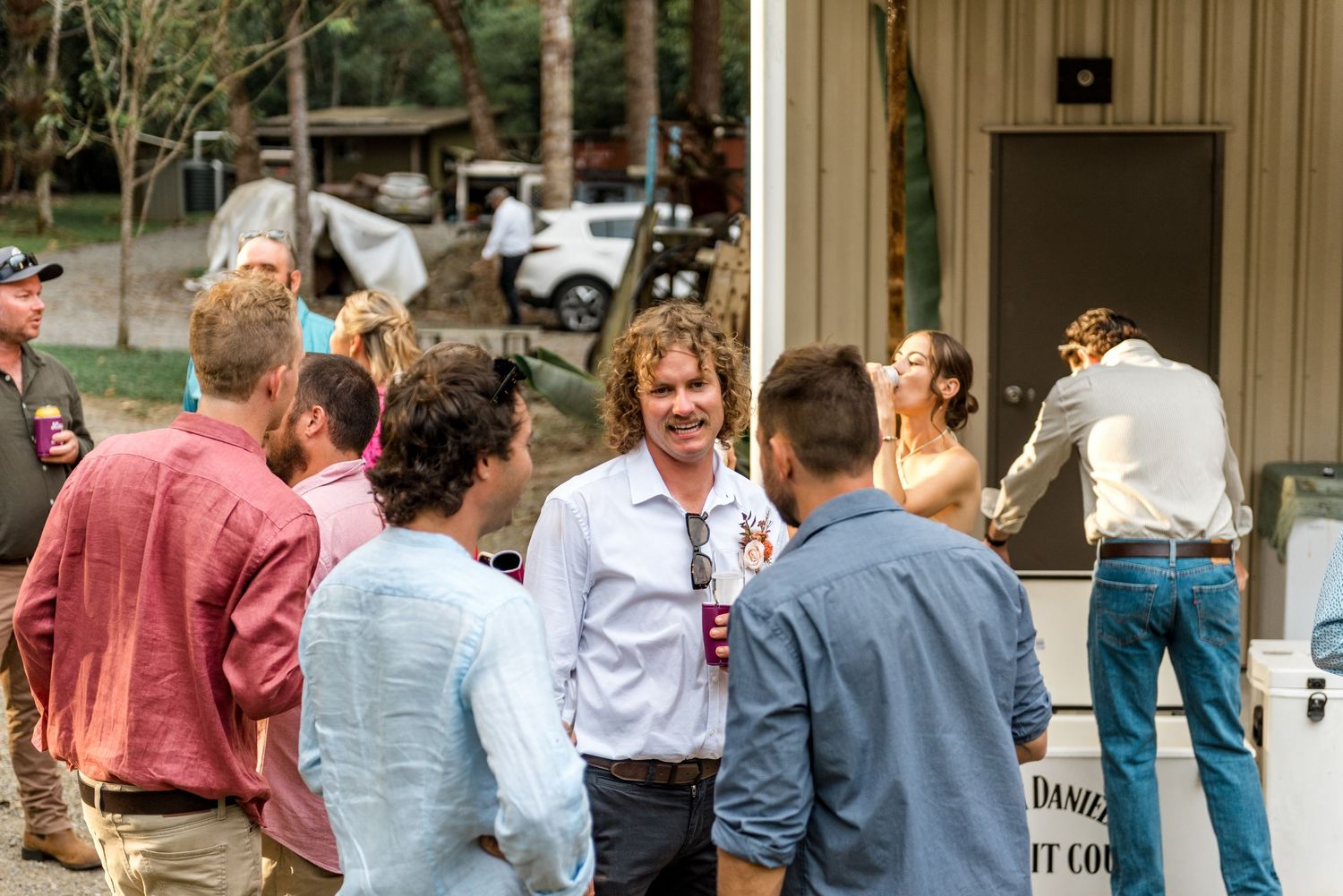 Group of guests socializing outdoors near white building at casual rustic wedding celebration.