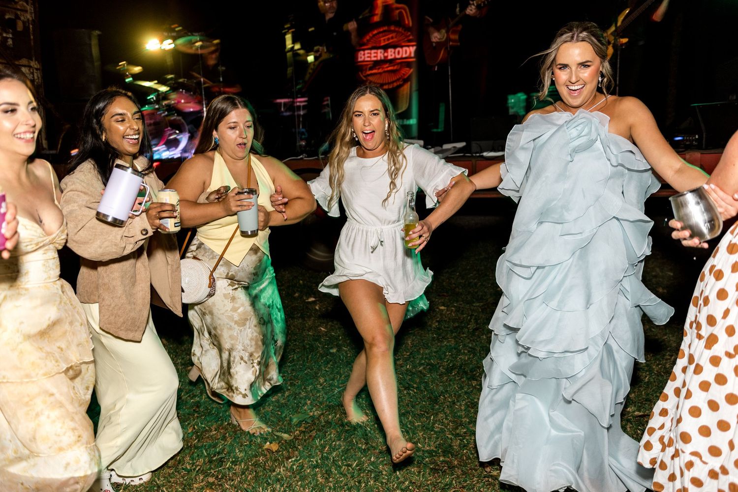Wedding guests in elegant dresses dancing together at outdoor evening reception celebration.