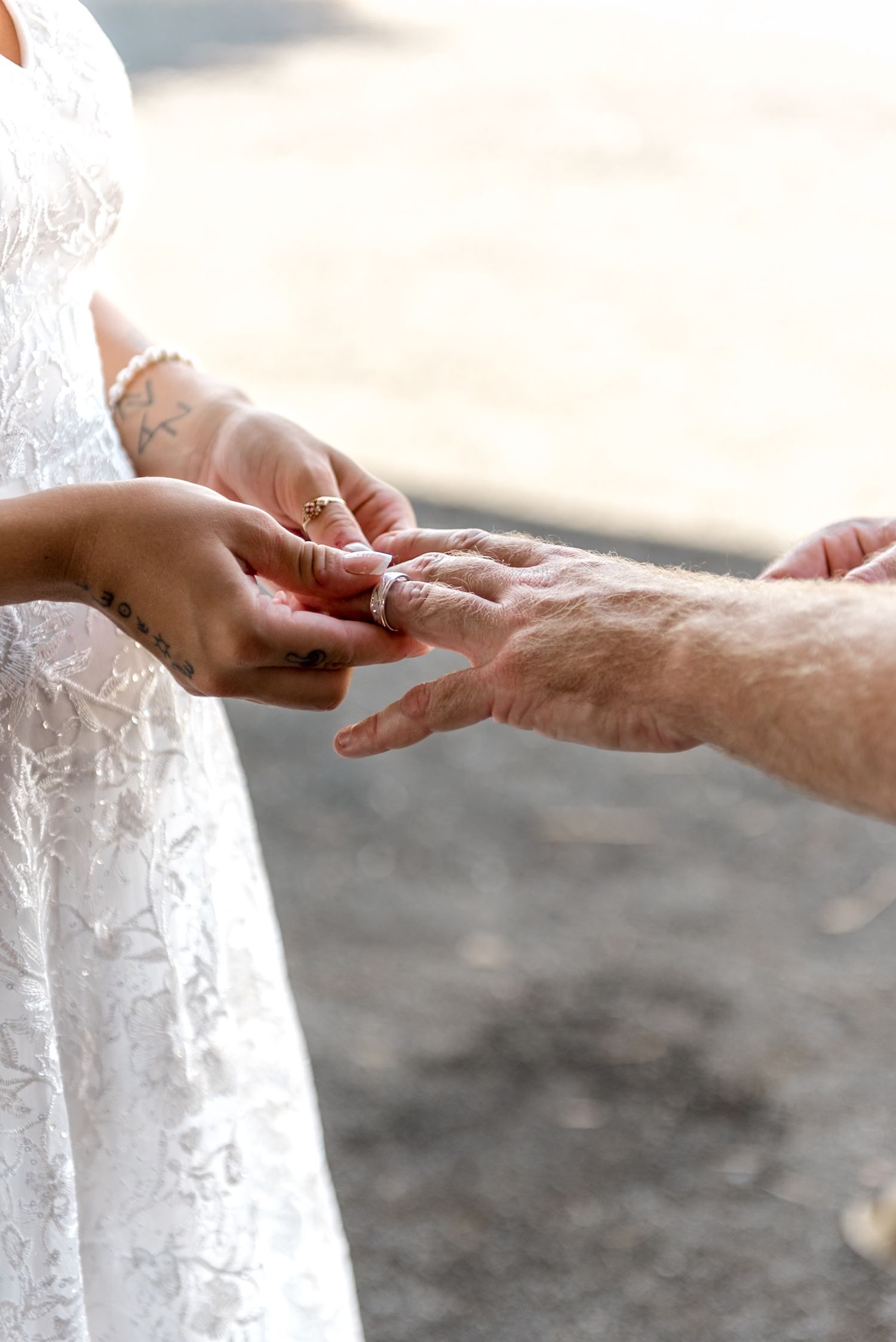 Groom sliding wedding band onto bride's finger during outdoor wedding ceremony.