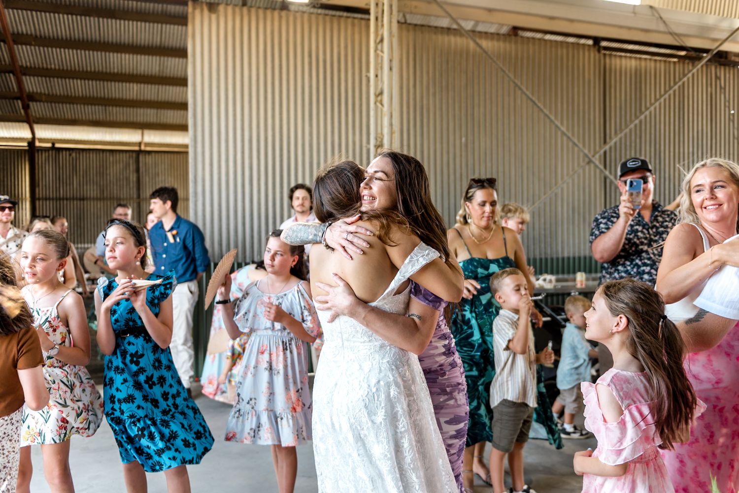 Bride joyfully hugs a guest surrounded by children at rustic barn wedding reception.